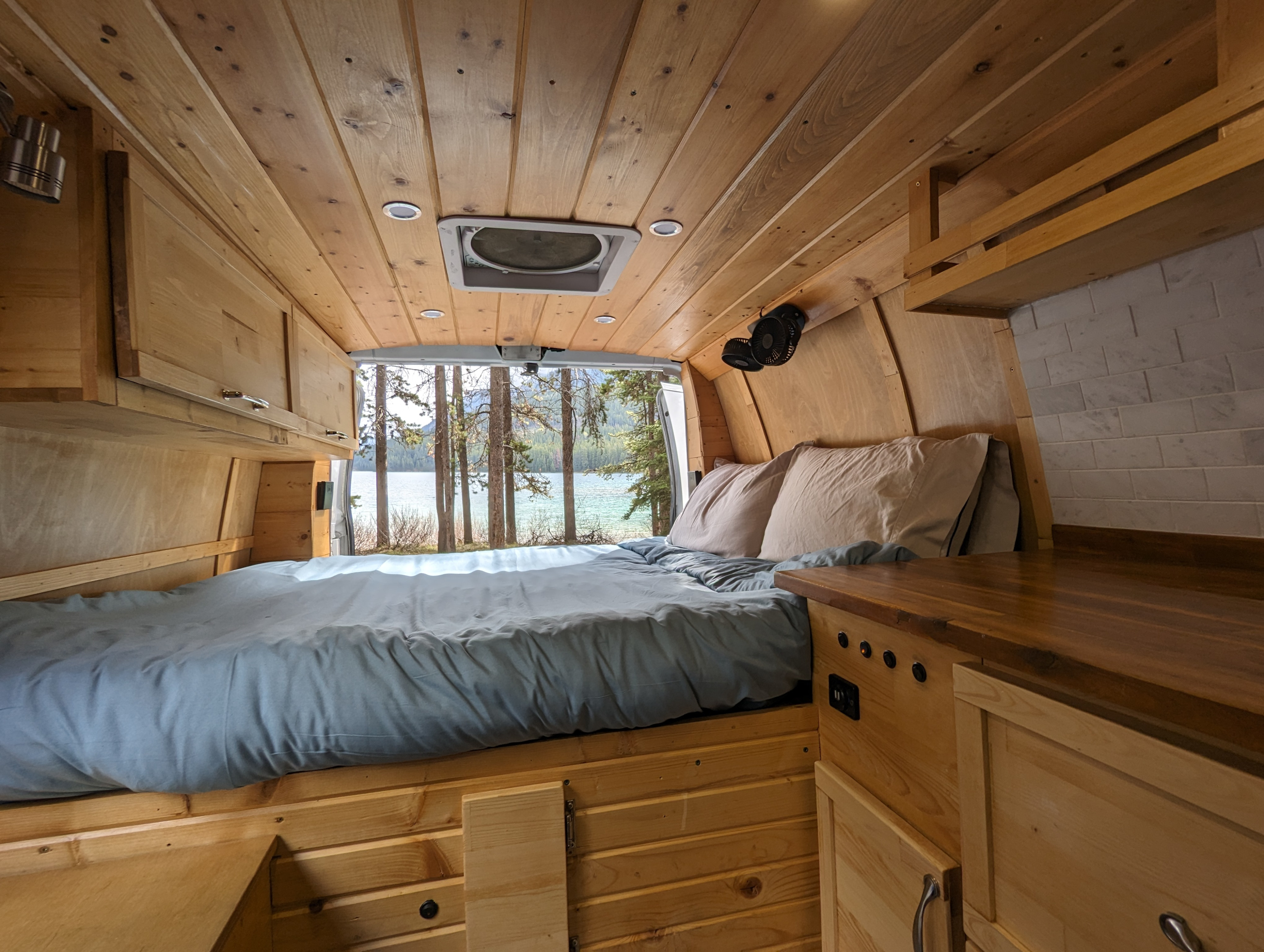 Inside a beautiful RV rental: a cozy wood-paneled bed area with a stunning lake and forest view.. Gmc Savanna 2015