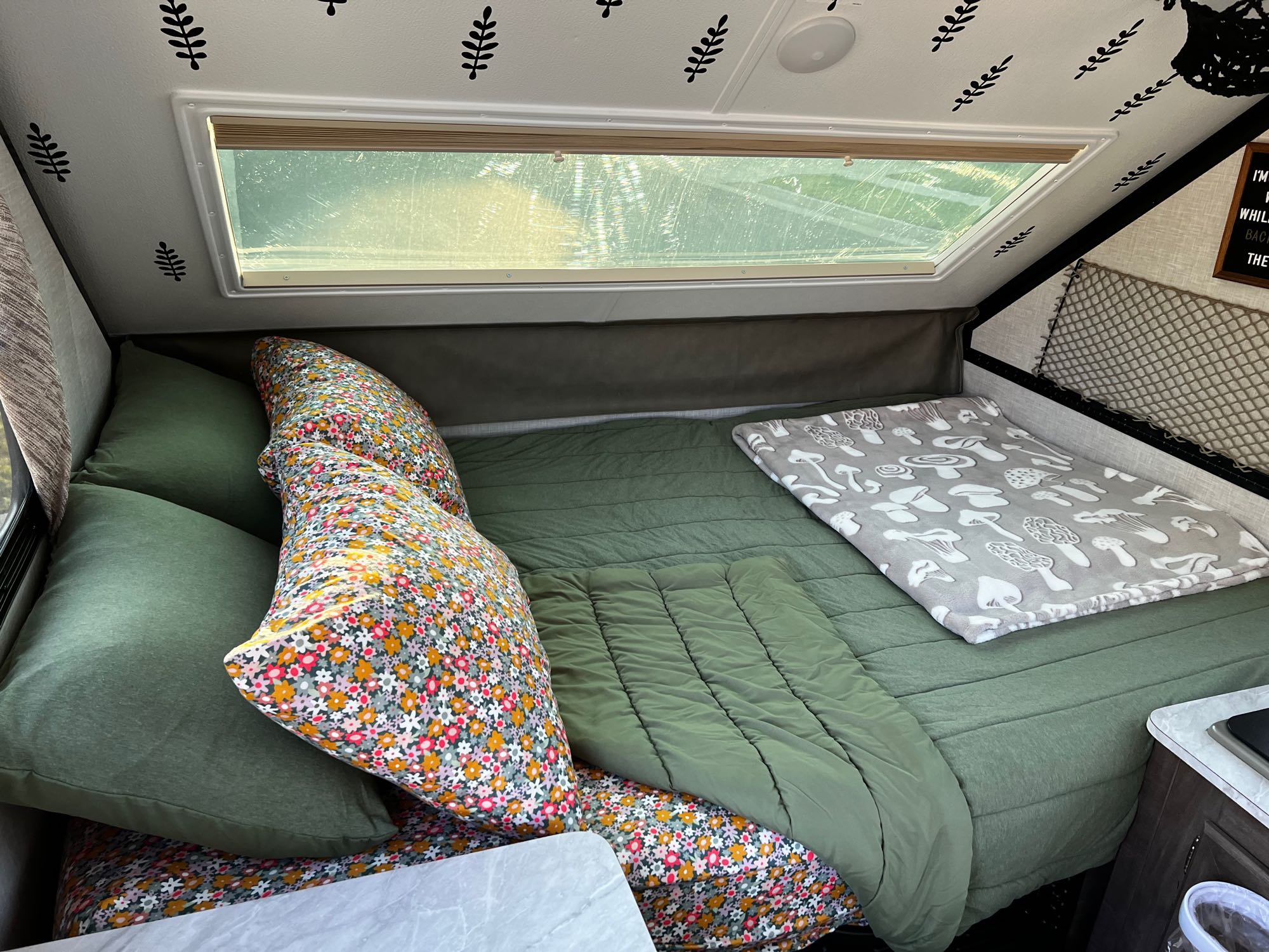 Cozy RV rental bedroom with nature-themed decor, green bedding, and a mushroom blanket. Ideal for camping.. Forest River Rockwood Premier 2023