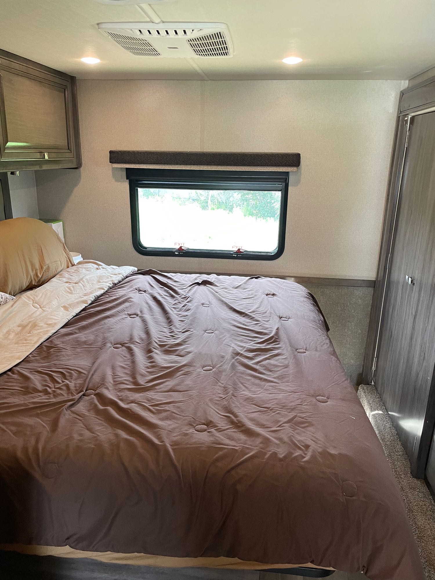 Cozy RV rental bedroom with a comfy bed, window, overhead AC, and wood-grain cabinets.. Holiday Rambler Admiral 2019