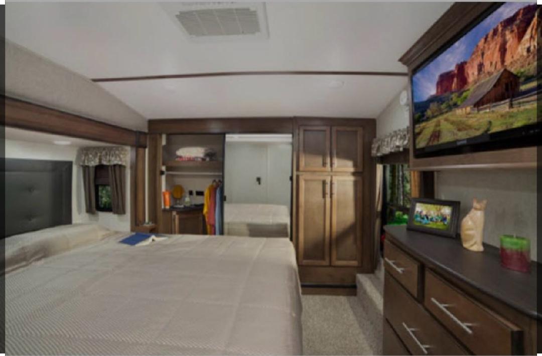 Spacious RV rental bedroom with a large bed, wooden cabinetry, and TV. Includes ample built-in storage.. Keystone Cougar 2020