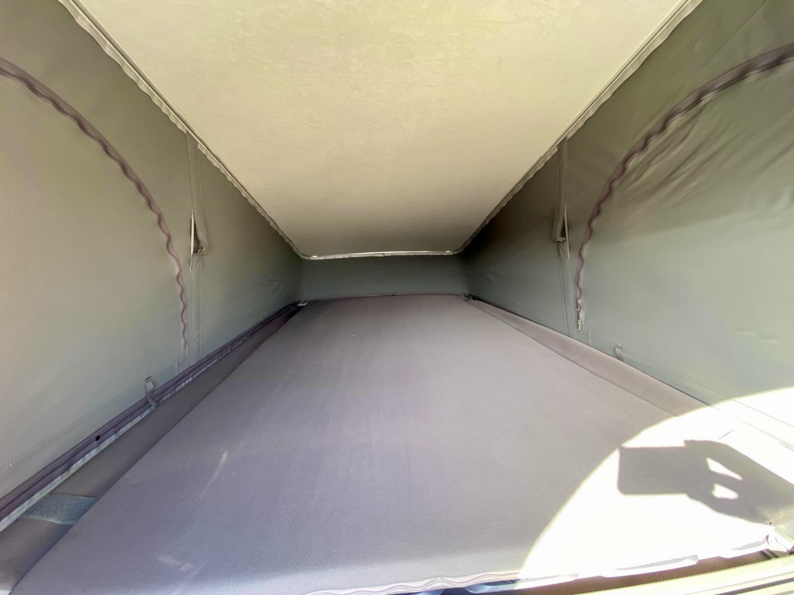 Inside an RV rental pop-top, a spacious sleeping area features a mattress and light-colored fabric walls and ceiling.. Adria Mode 2024