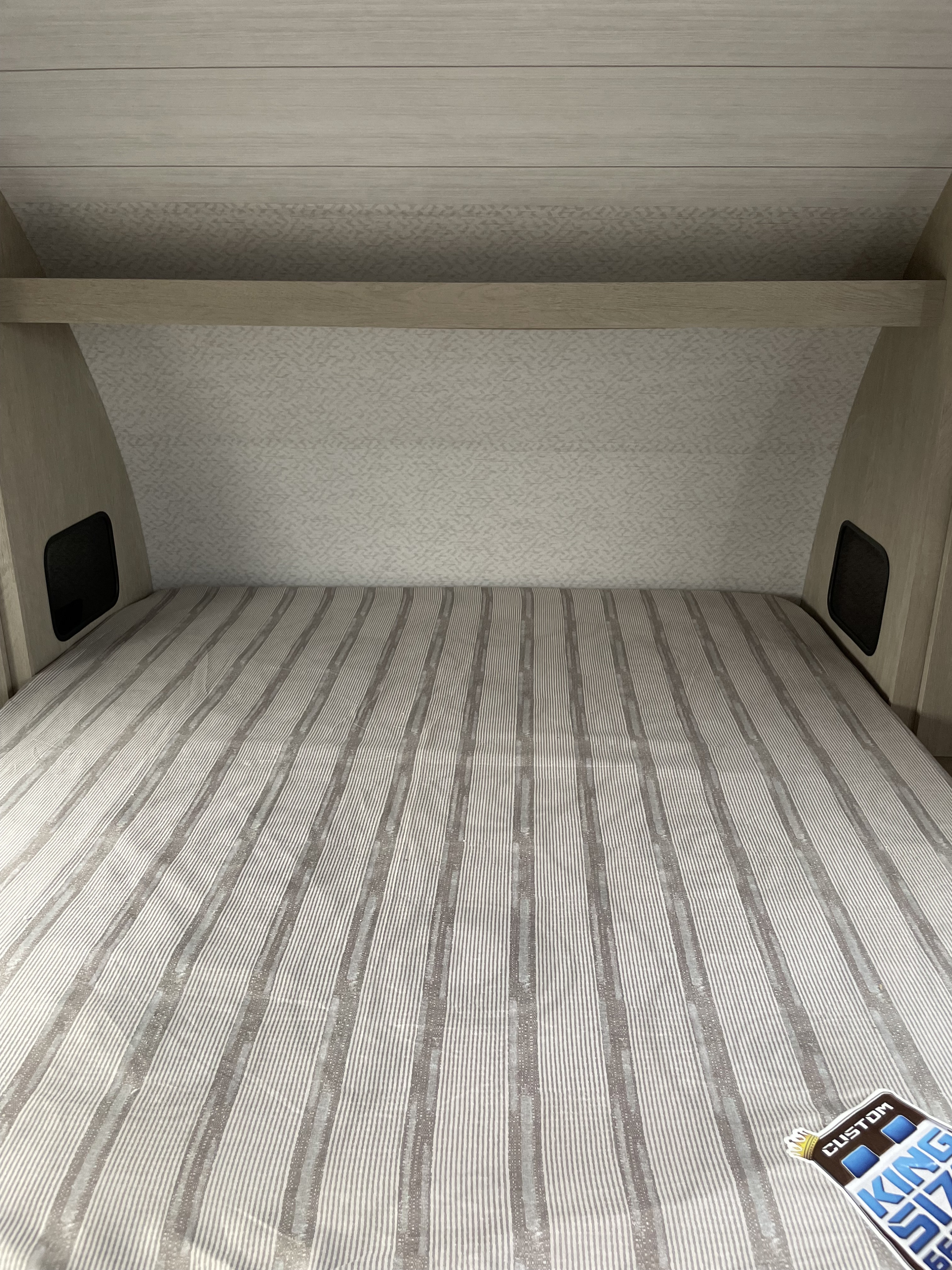 RV rental sleeping area featuring a striped bed, light wood paneling, and practical built-in side storage.. Forest River Wildwood X-Lite 2023