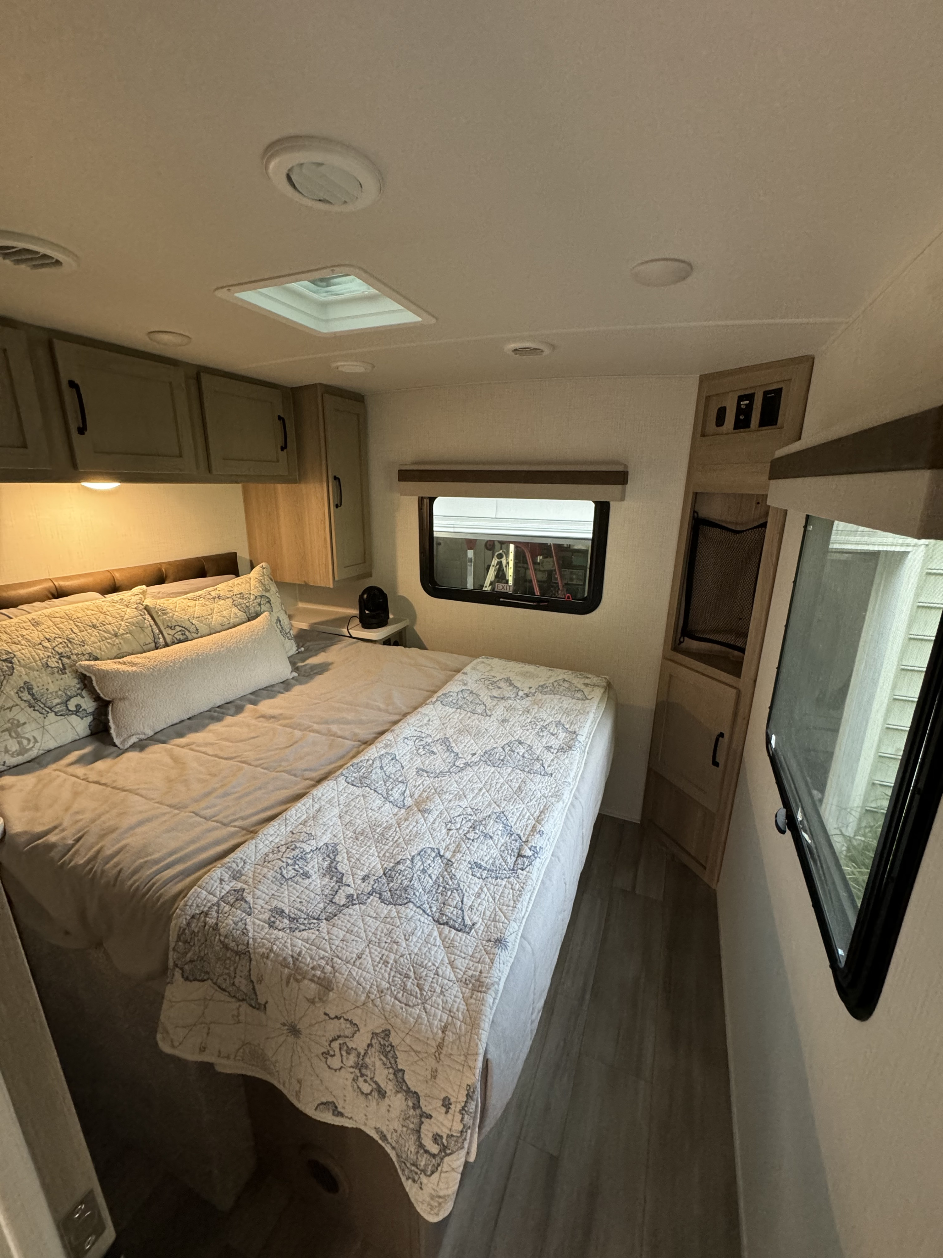 Inside an RV rental: a cozy bedroom features a bed with map-patterned quilt, overhead cabinets, windows, and wood-look floor.. Forest River Rockwood Mini Lite 2024