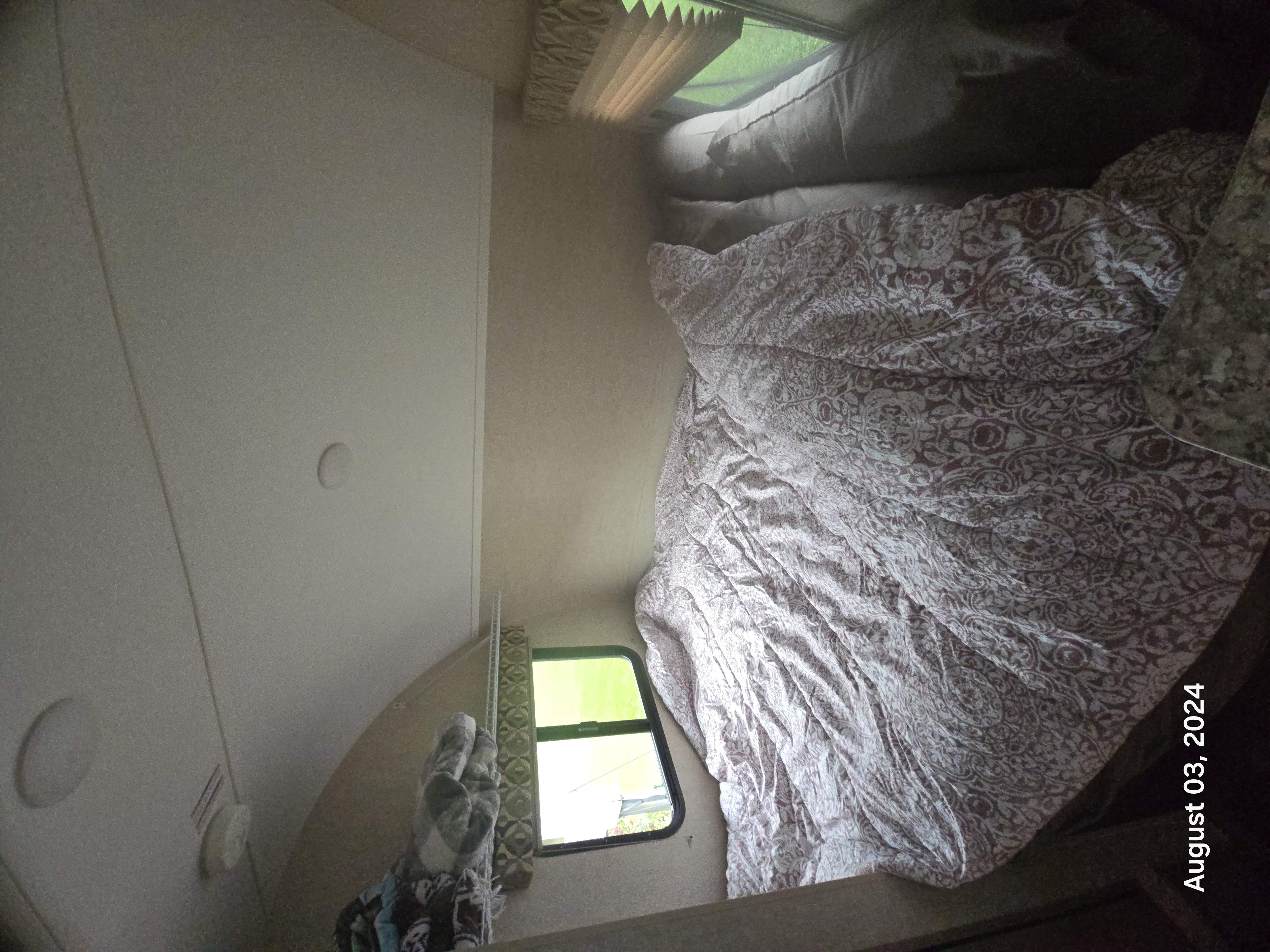 Inside an RV rental: a cozy bedroom with a patterned bed, window, and pleated blinds.. Starcraft Satellite 2017