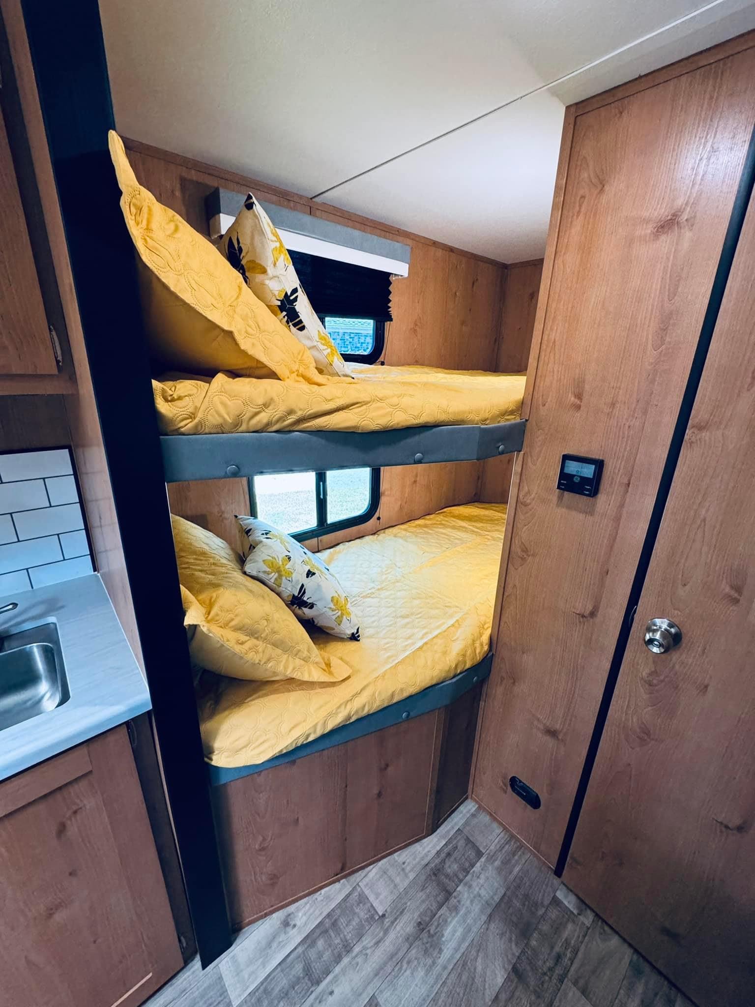 Inside an RV rental: Bright yellow bunk beds with patterned pillows, adjacent to a kitchenette with a sink and white tile backsplash.. Riverside RV Retro 2023