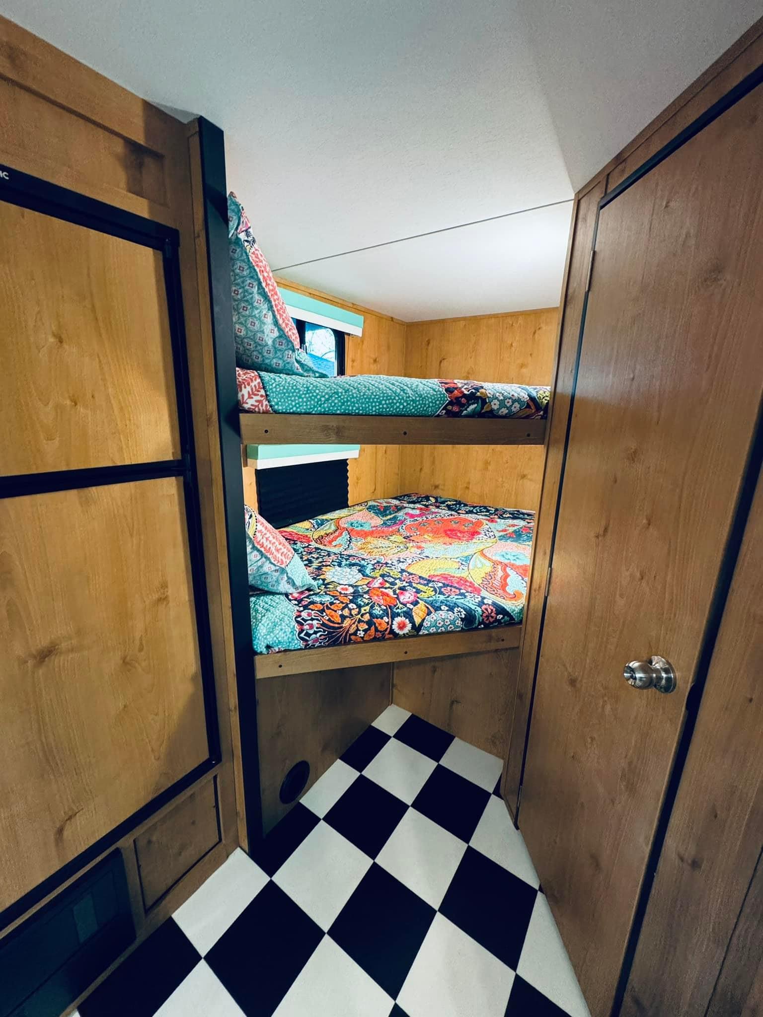 Cozy RV rental interior with colorful stacked bunk beds & checkered floor, ideal for family travel.. Riverside RV Retro 2023