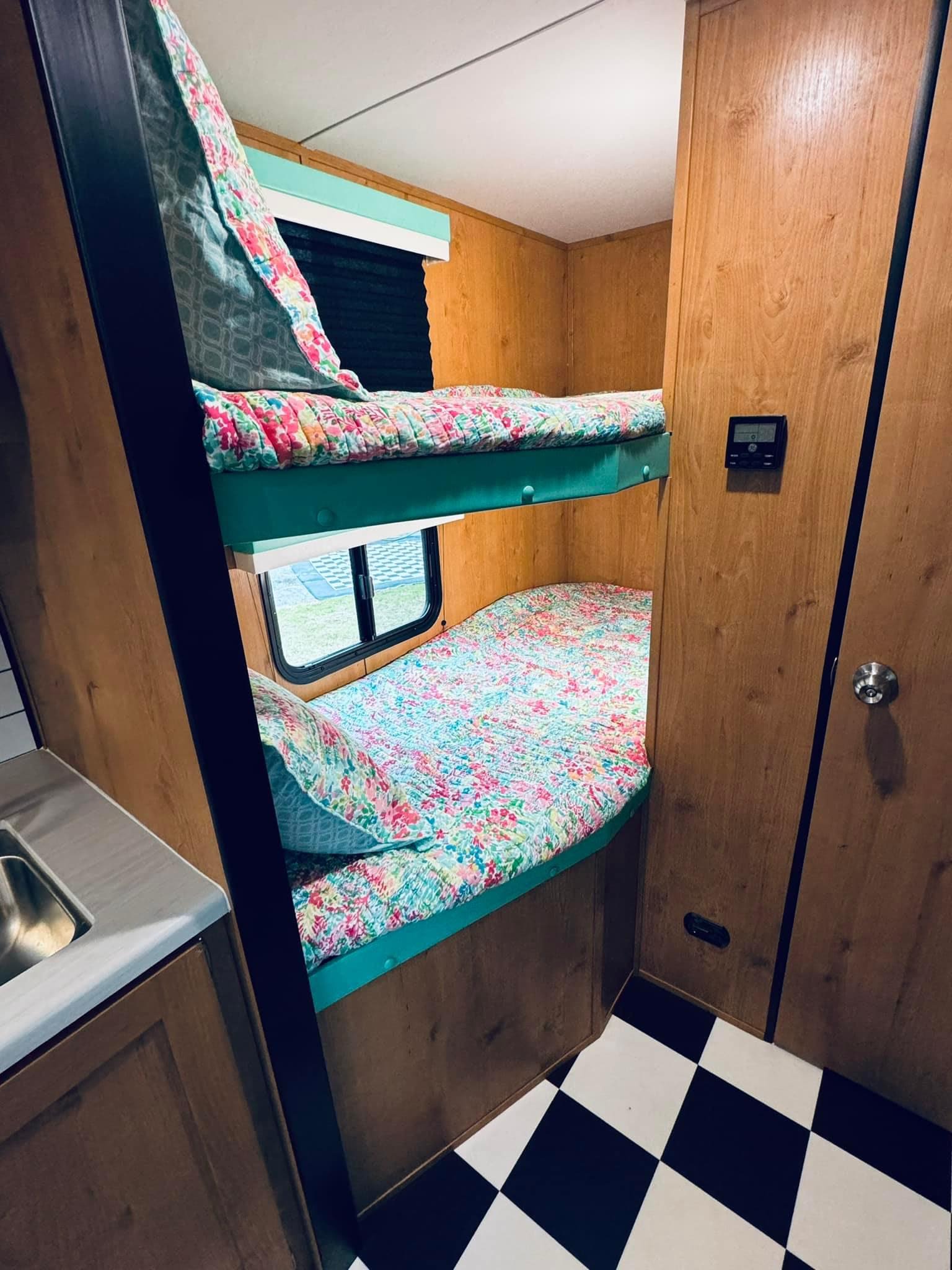 Cozy bunk beds in an RV rental, featuring floral bedding, wood paneling, and a black & white checkered floor.. Riverside RV Retro 2023