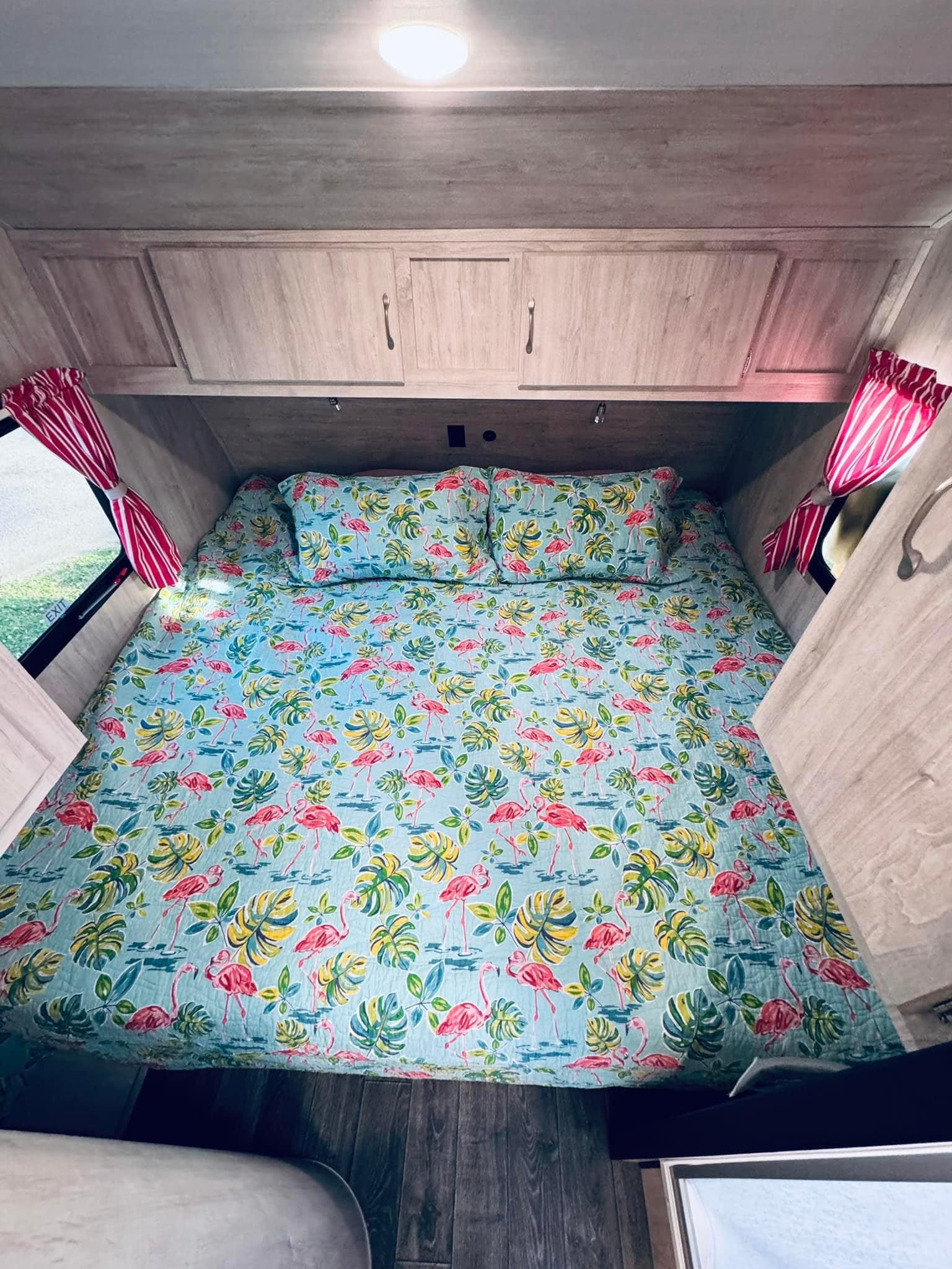 Comfortable RV rental bedroom with a vibrant tropical flamingo bedspread, built-in cabinets, and window curtains.. Gulf Stream Vintage Cruiser 2024