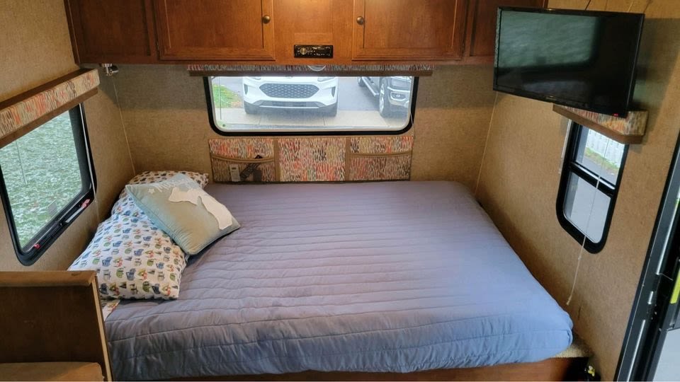 Cozy RV rental bedroom with a comfy bed, overhead cabinets, windows, and TV, ready for your next adventure.. Spree Escape 2016