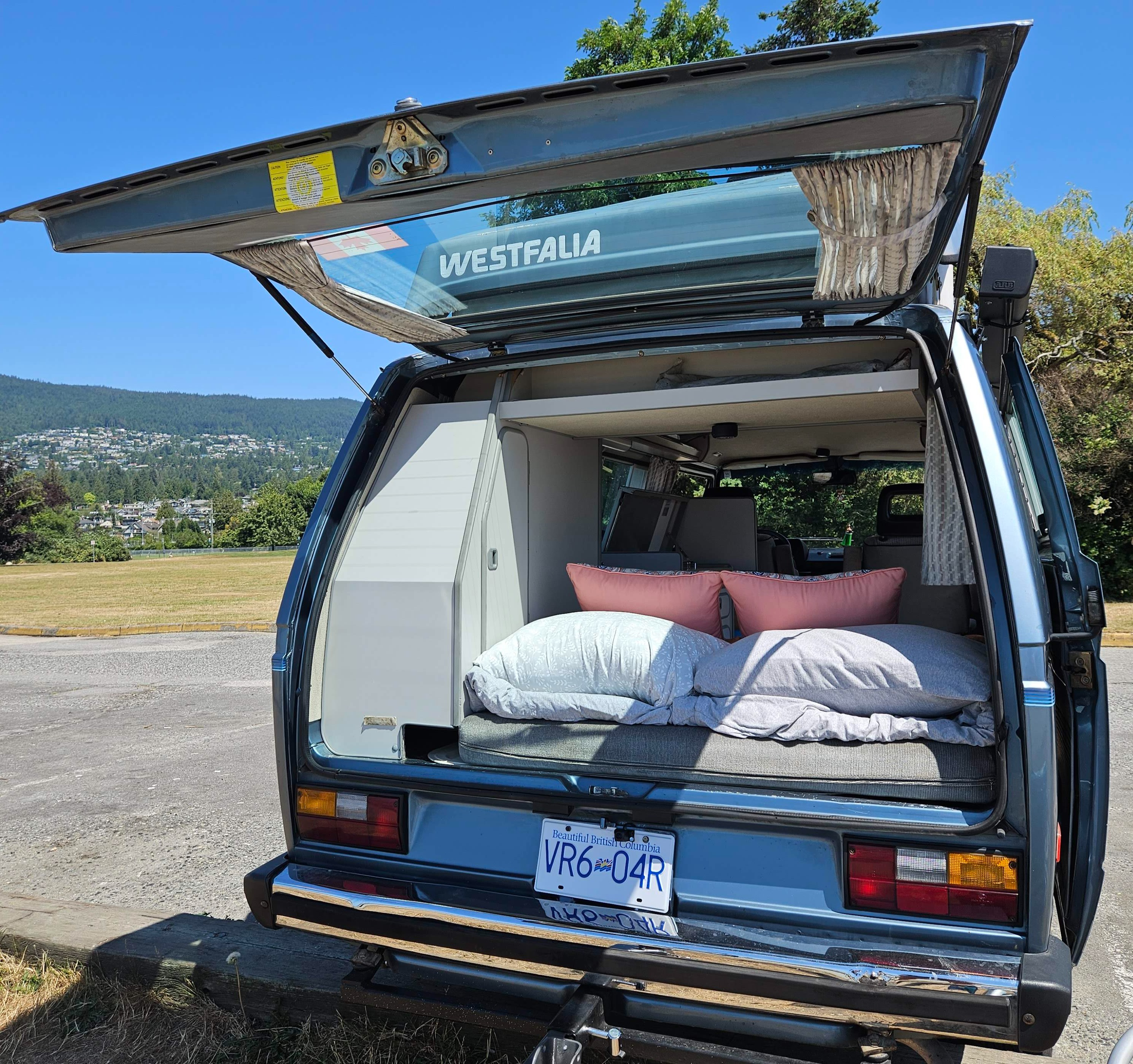 This blue Westfalia camper van, with its rear hatch open to reveal a cozy bed, is perfect for an RV rental adventure in BC.. Westfalia T3 Westfalia 1987
