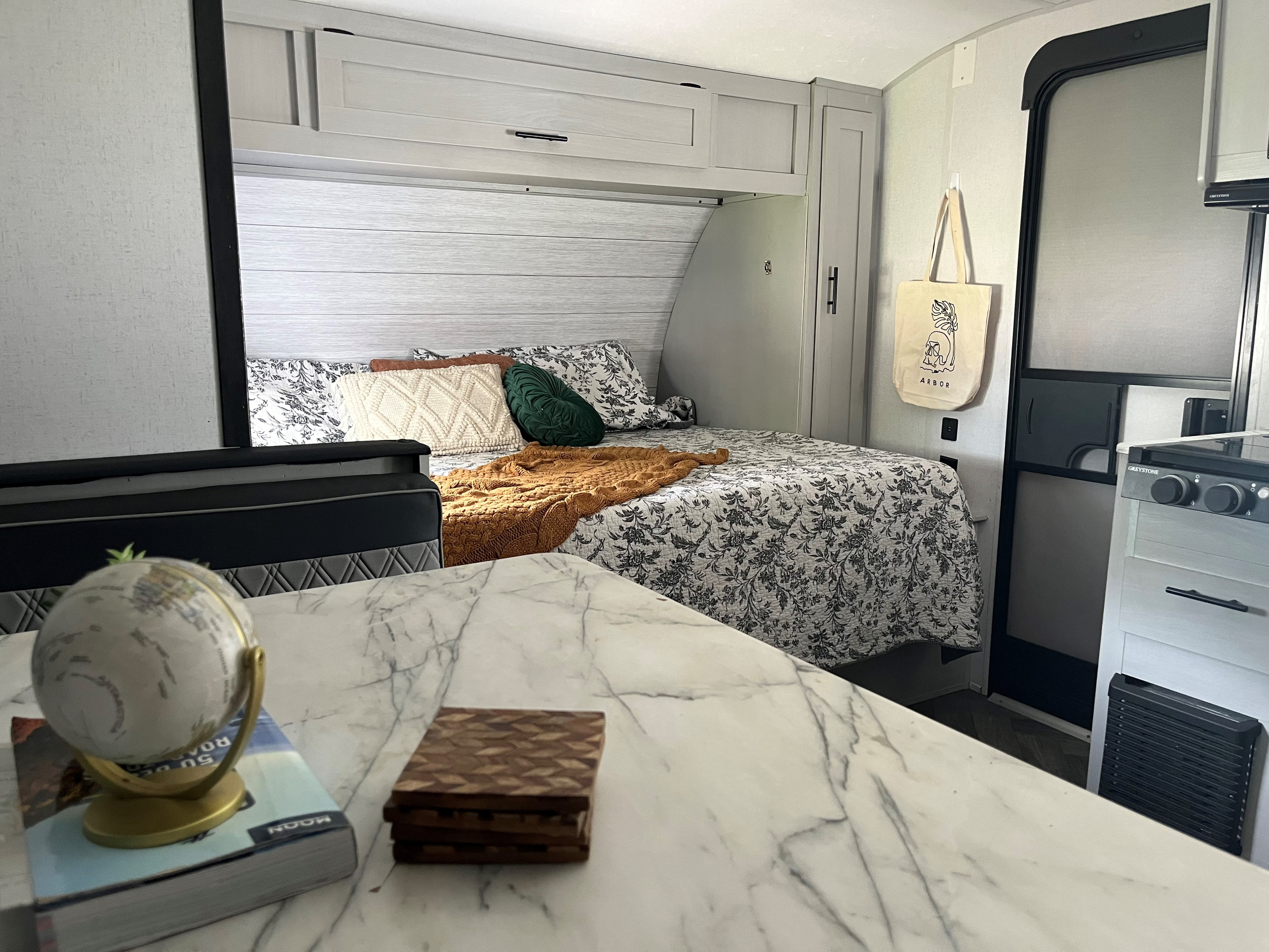 Inside a stylish RV rental: a cozy bed with patterned bedding, a compact kitchen area, and a marble countertop.. Forest River Wildwood FSX 2021
