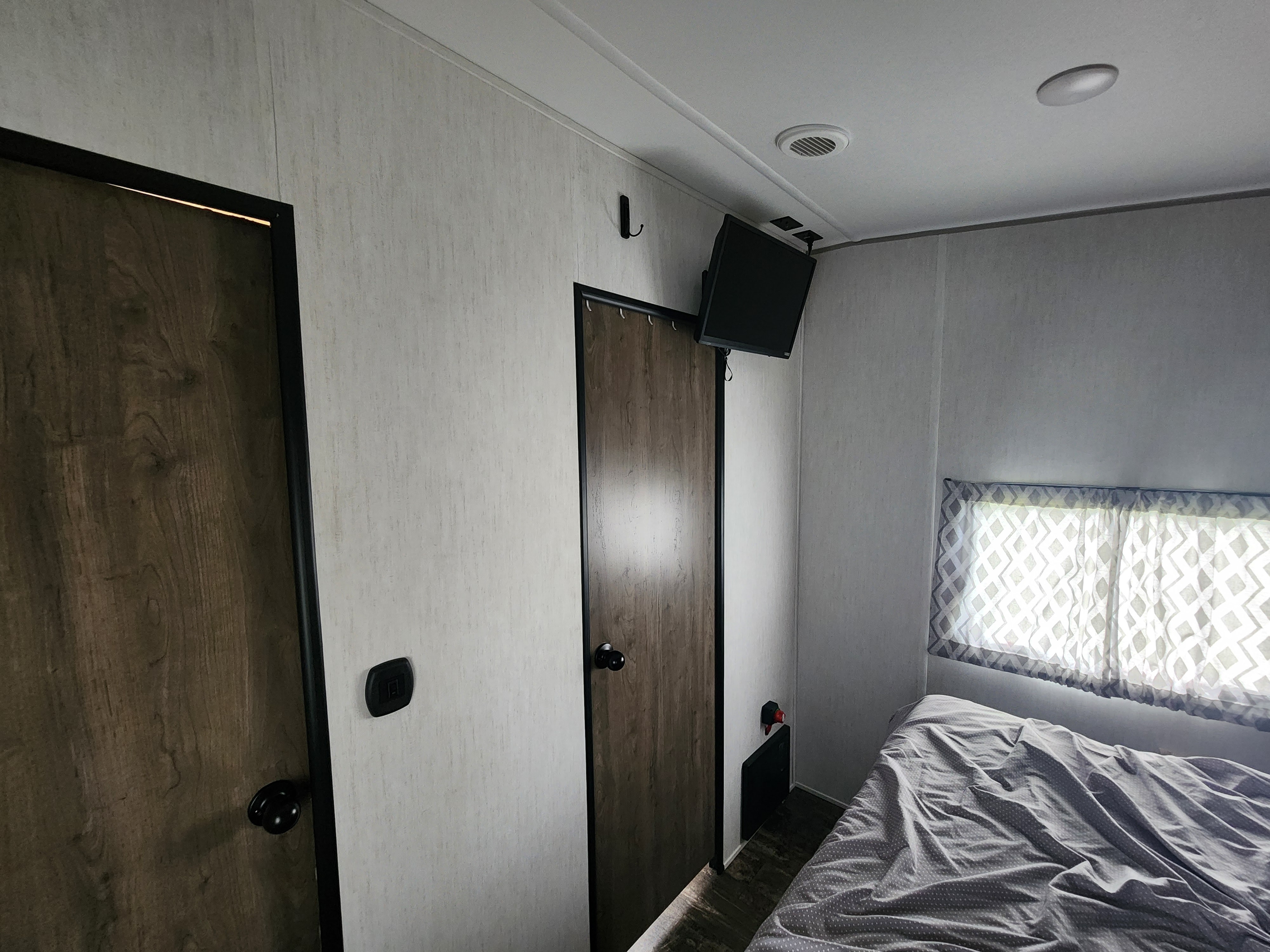 RV rental bedroom interior: Features wood doors, polka-dot bed, window, and wall-mounted TV.. Forest River Wolf Pack 2023