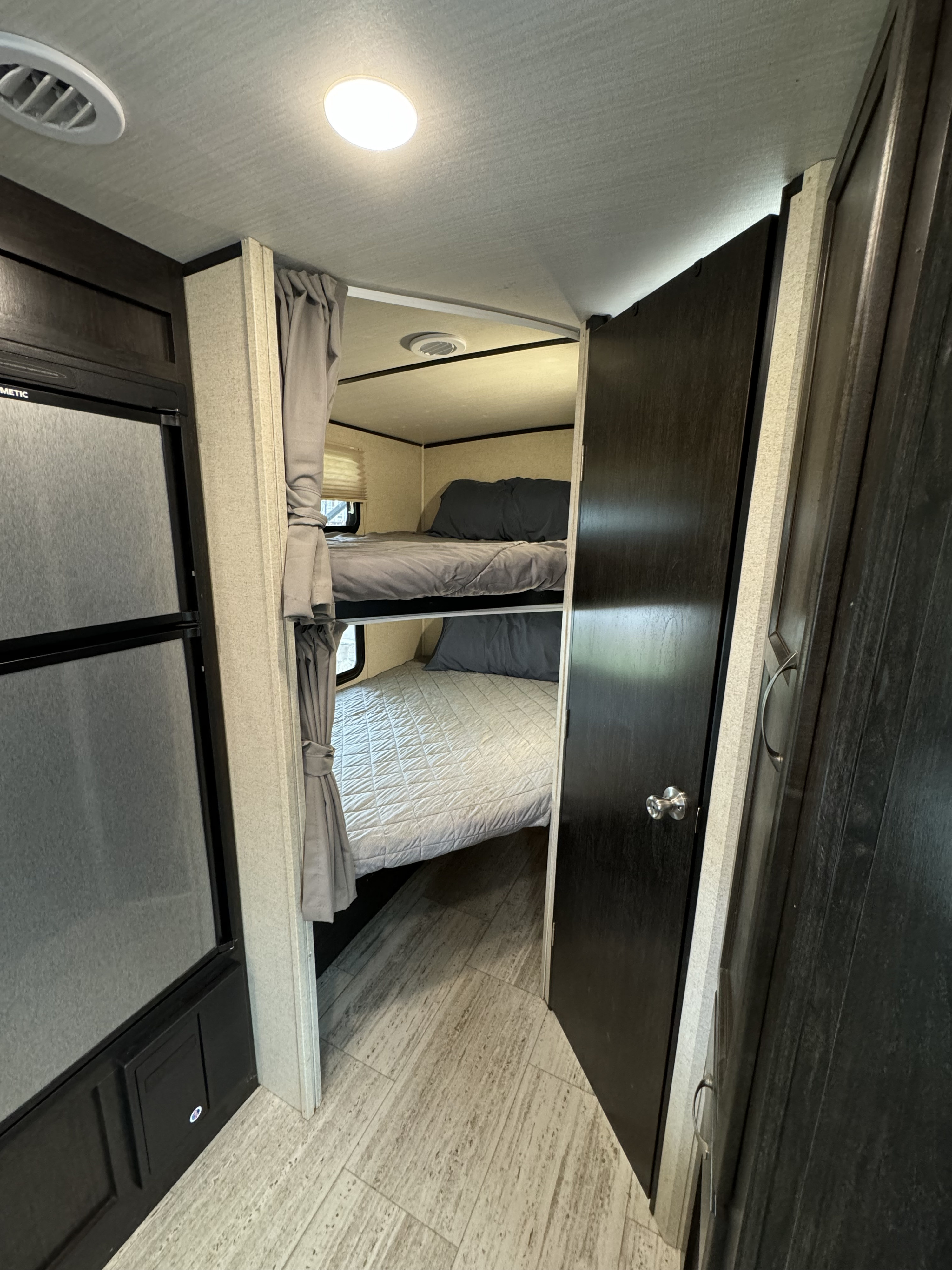 This RV rental offers a compact interior with bunk beds, grey bedding, a refrigerator, and wood-look flooring, perfect for travel.. Forest River Coachmen Spirit Ultra Lite 2020