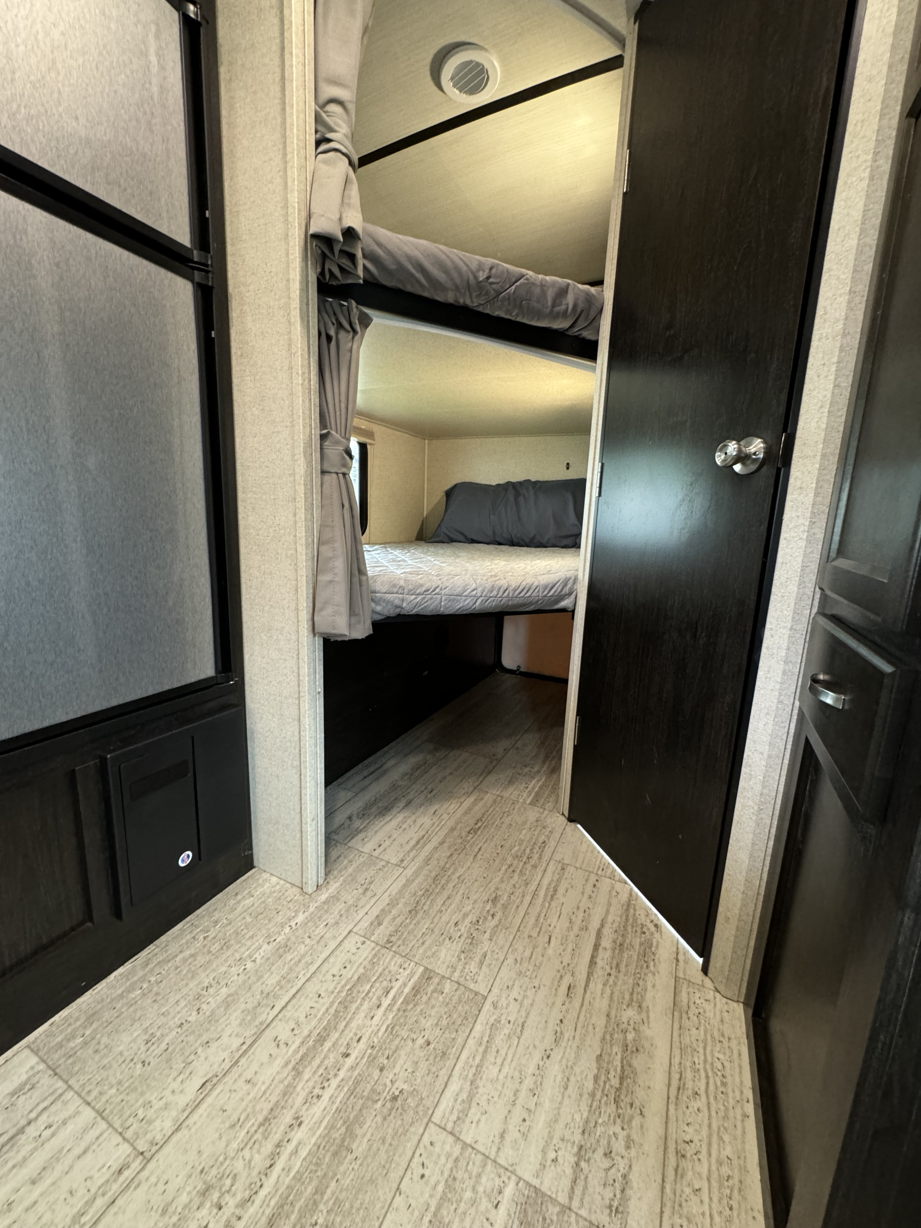 This RV rental interior features bunk beds with gray bedding, a hallway, and dark wood accents. Ideal for family trips.. Forest River Coachmen Spirit Ultra Lite 2020