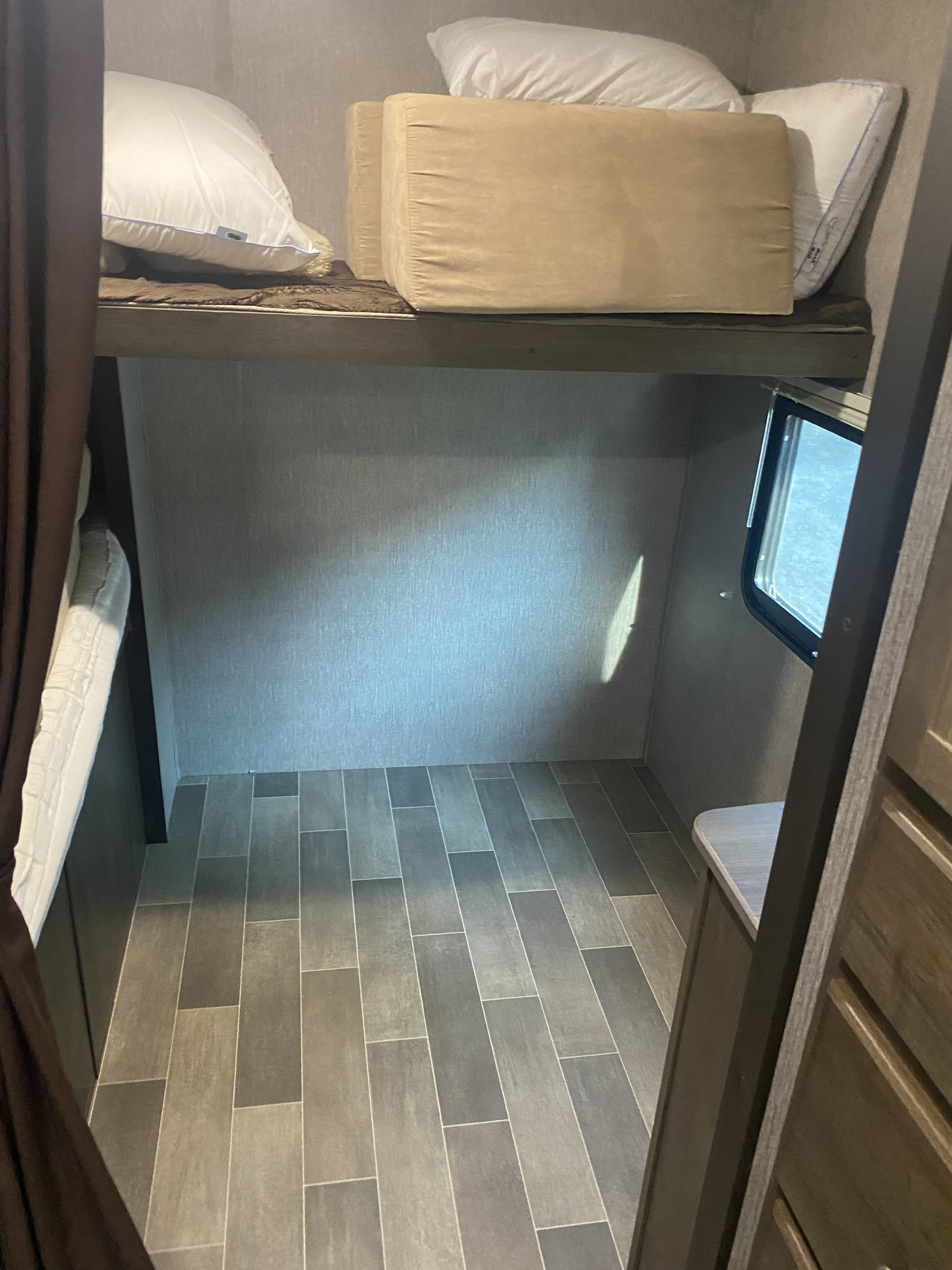 RV rental bunk bed interior: Cozy sleeping area with pillows on top, ample floor space below, a small window, and modern tile flooring.. Keystone RV Coleman Lantern edition 295QB 2019