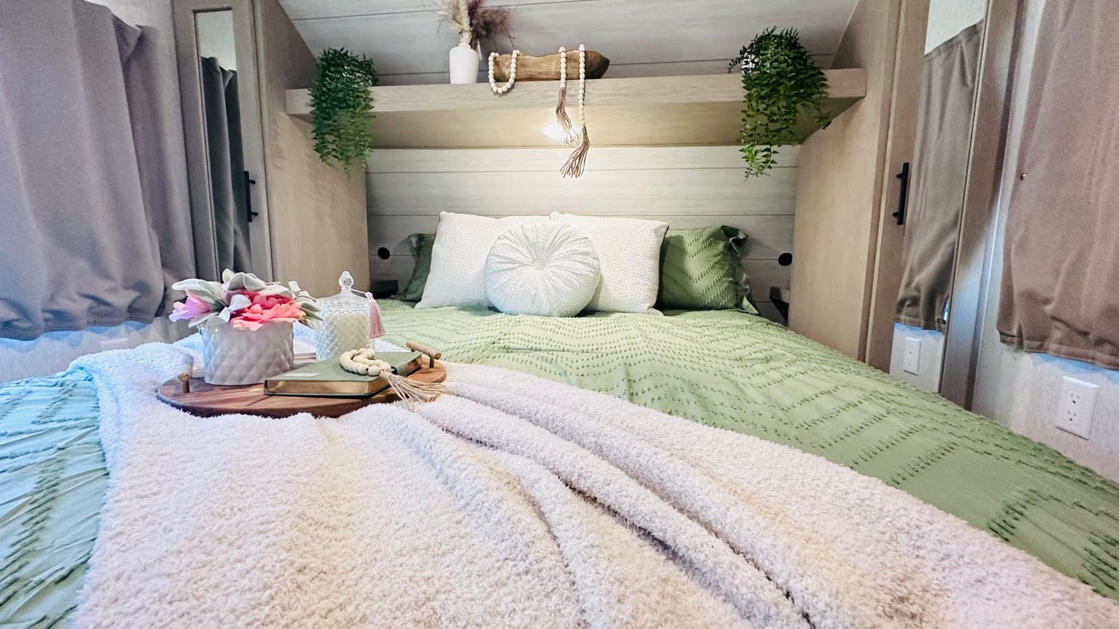 Experience comfort in this cozy RV rental bedroom, featuring green bedding, plants, and chic decor.. Forest River Wildwood X-Lite 2024