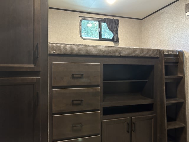 Dark wood RV rental interior with a bunk bed, drawers, shelves, and cabinets. A small window offers a view outside.. Jayco Eagle 312 BHOK 2024