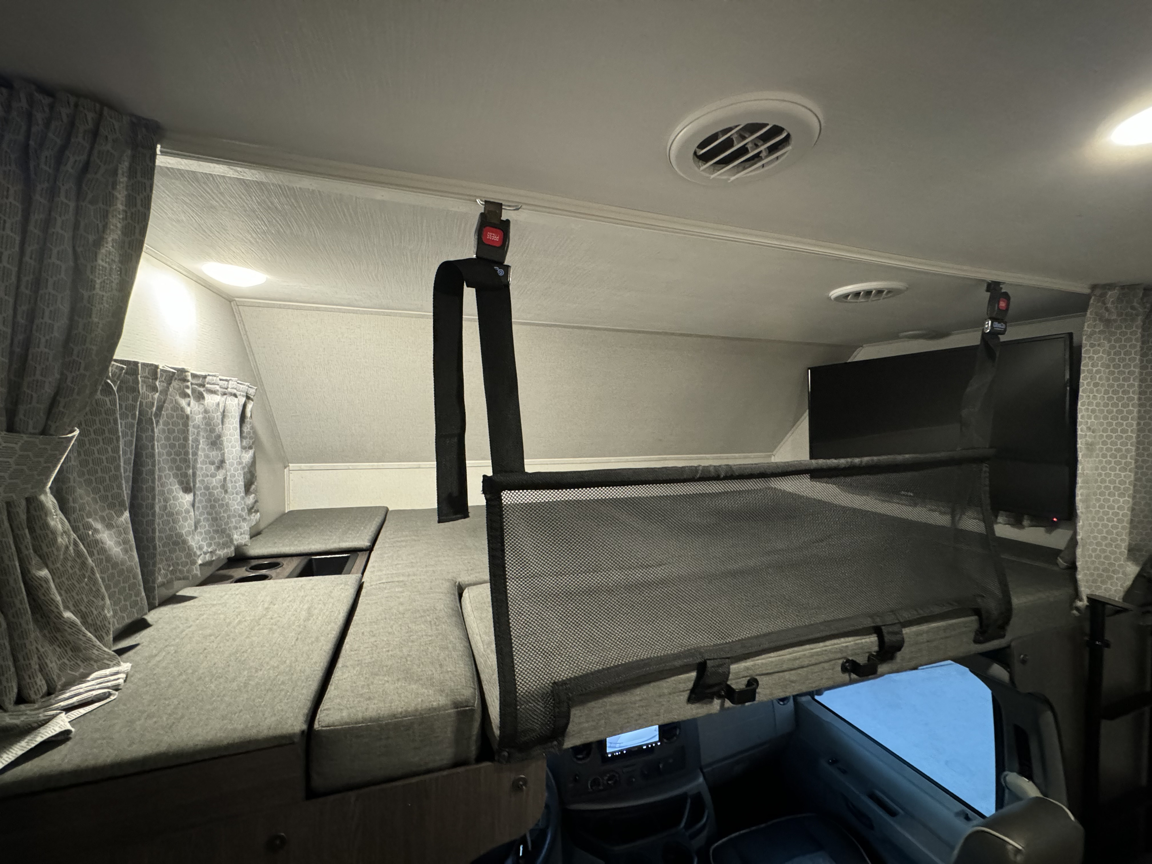 Cozy cab-over bunk bed with safety net inside an RV rental. Features ceiling vents & curtains for comfortable travel.. Forester LE 2022