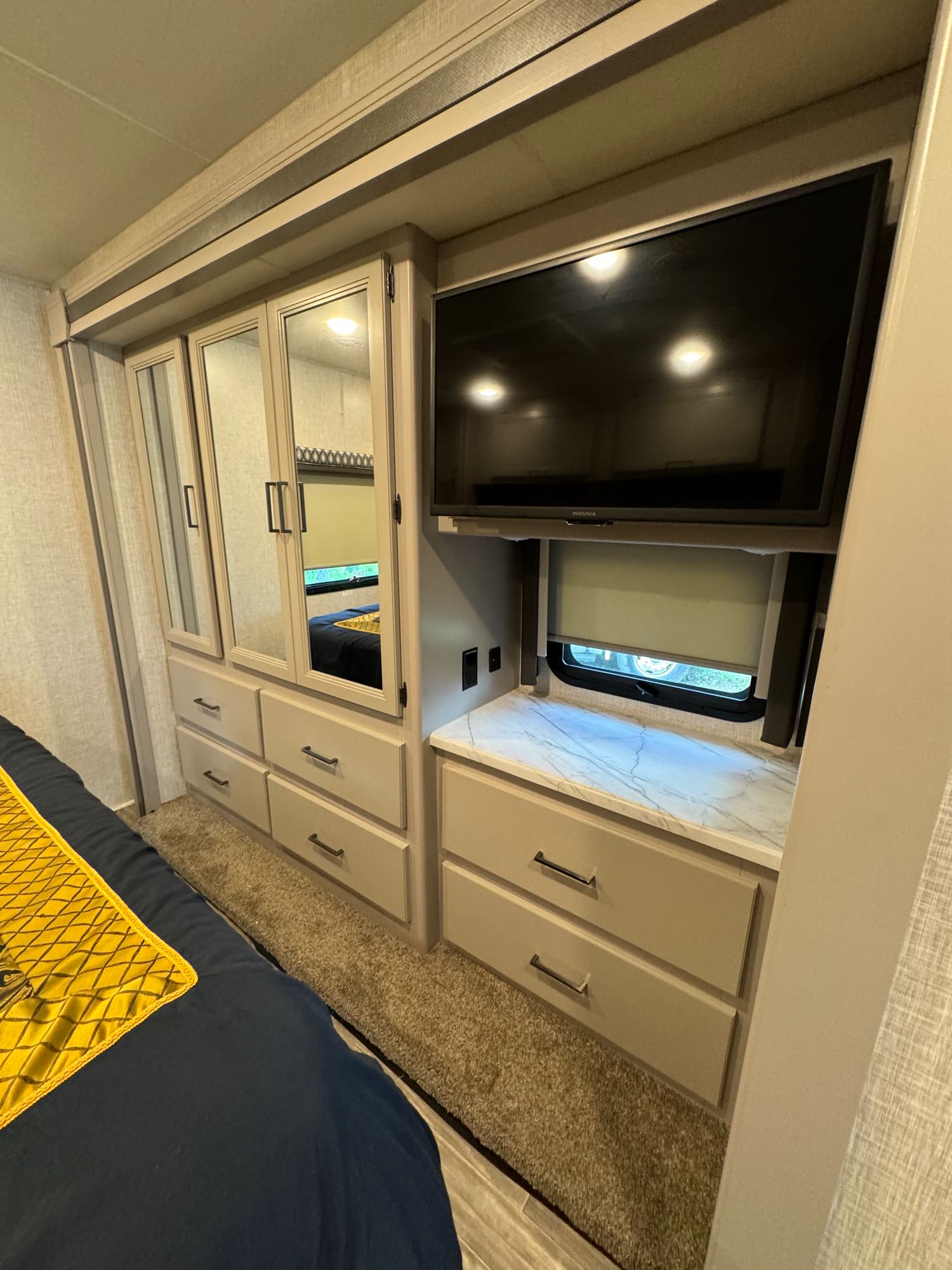 Explore this RV rental bedroom: cozy space with built-in mirrored closet, drawers, TV, and window shade. Comfortable and functional.. Thor Hurricane 2023