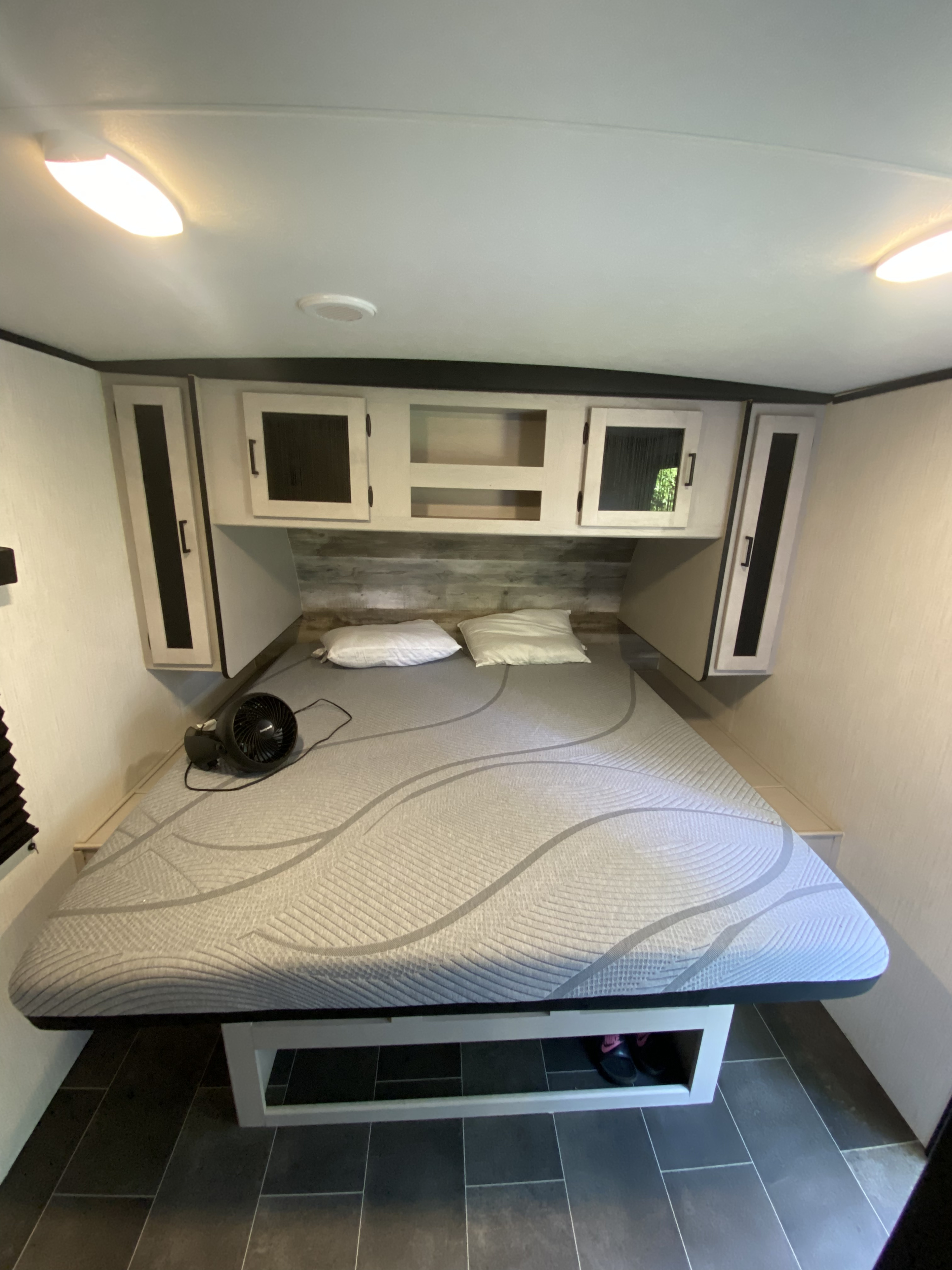 RV rental bedroom with patterned queen bed, two pillows, fan, and ample overhead storage. Dark tiled floor completes the cozy space.. Heartland RVs Mallard 2022