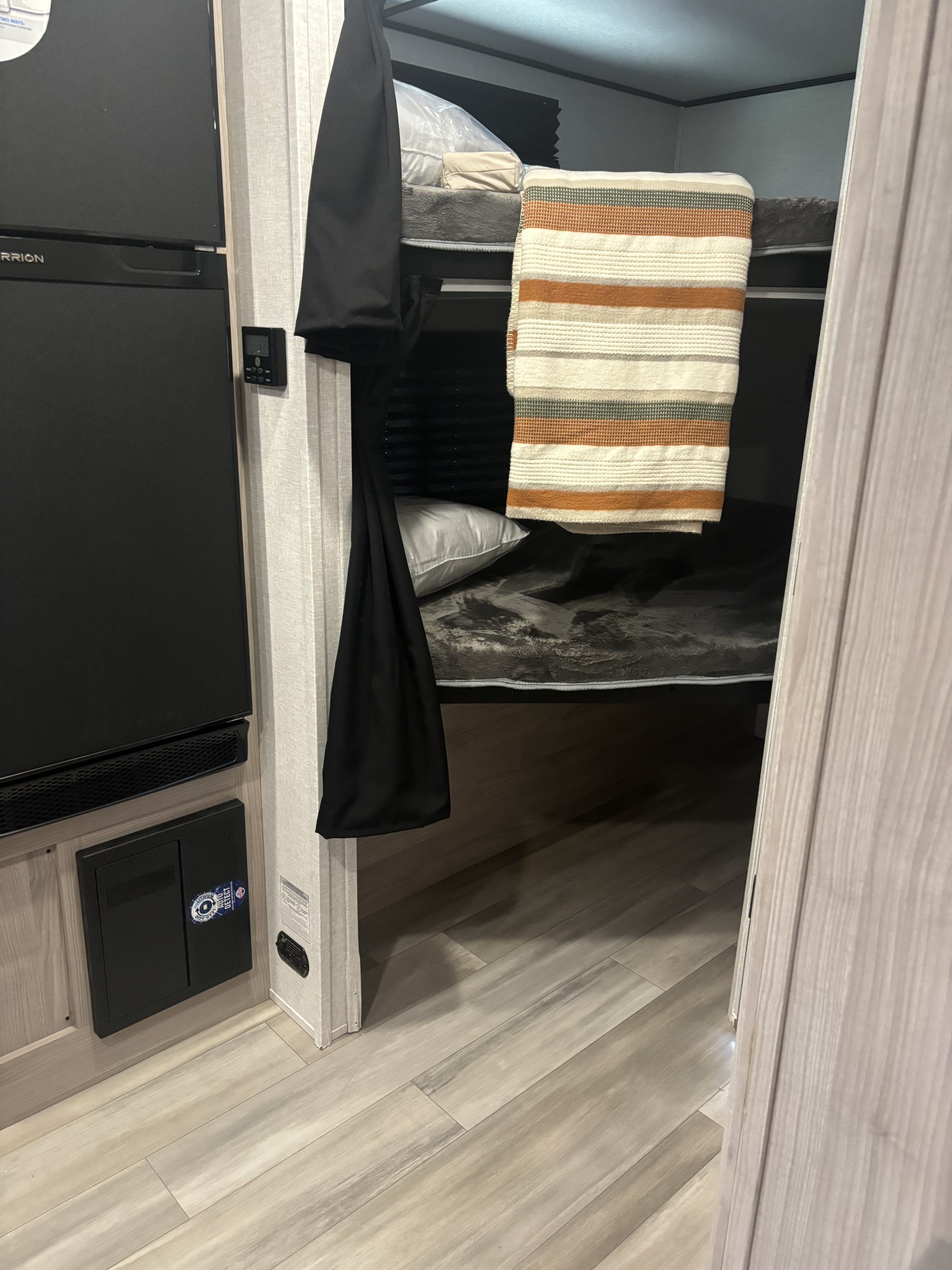 RV rental bunk bed area featuring striped blanket; refrigerator and control panel visible on the left.. Coachmen Northern Spirit 2146 BHX 2023