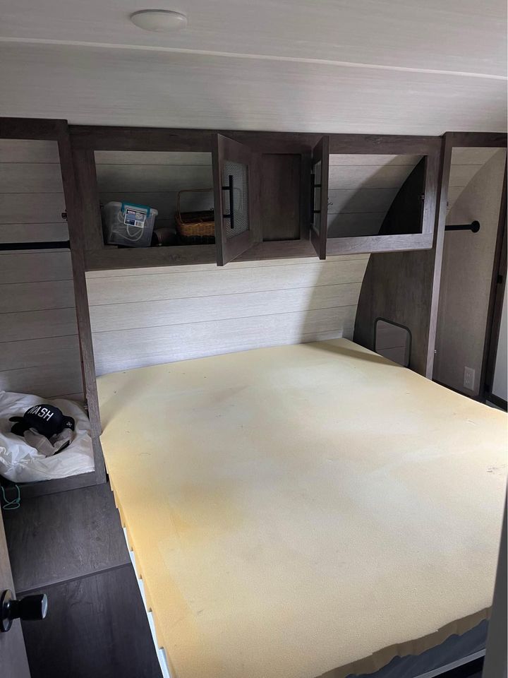 Basic RV rental bedroom featuring a foam mattress, open overhead storage, and light wood interior paneling.. Forest River Wildwood 2021