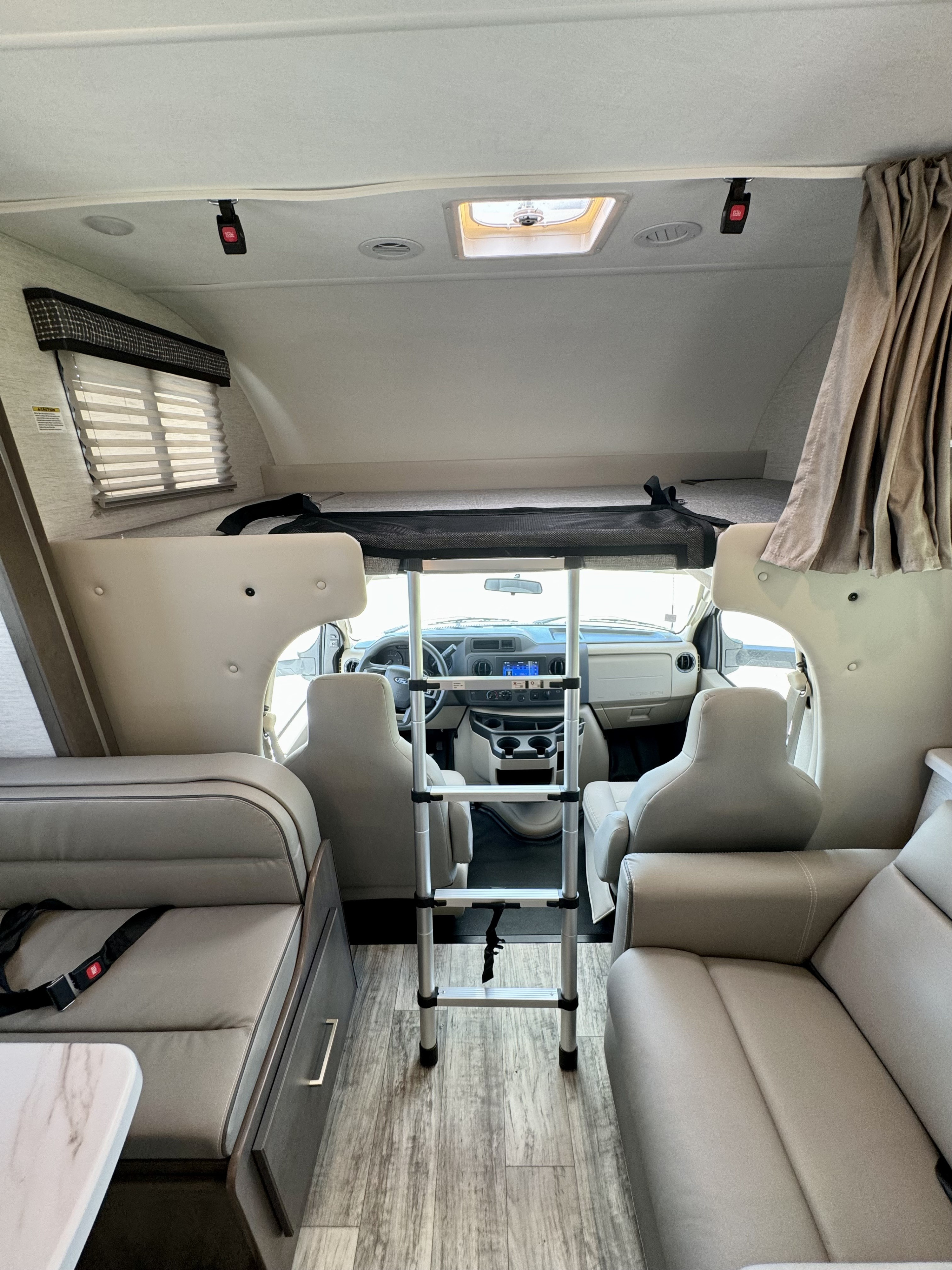 Looking forward in an RV rental: cockpit, over-cab bunk with ladder, dinette on left, lounge on right.. Thor Chateau 2024