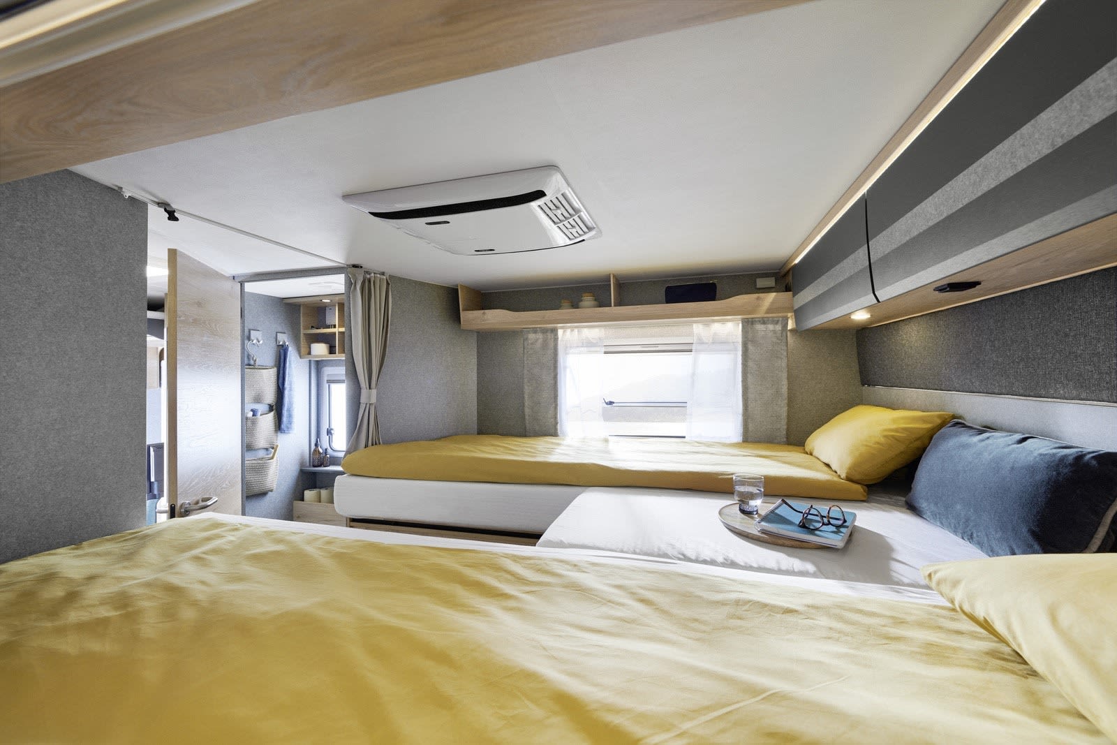 Bright, modern RV rental bedroom. Features two comfortable beds, overhead AC, and a scenic window view. Your cozy home on wheels.. Dethleffs Just Go T 7055 EB 2023