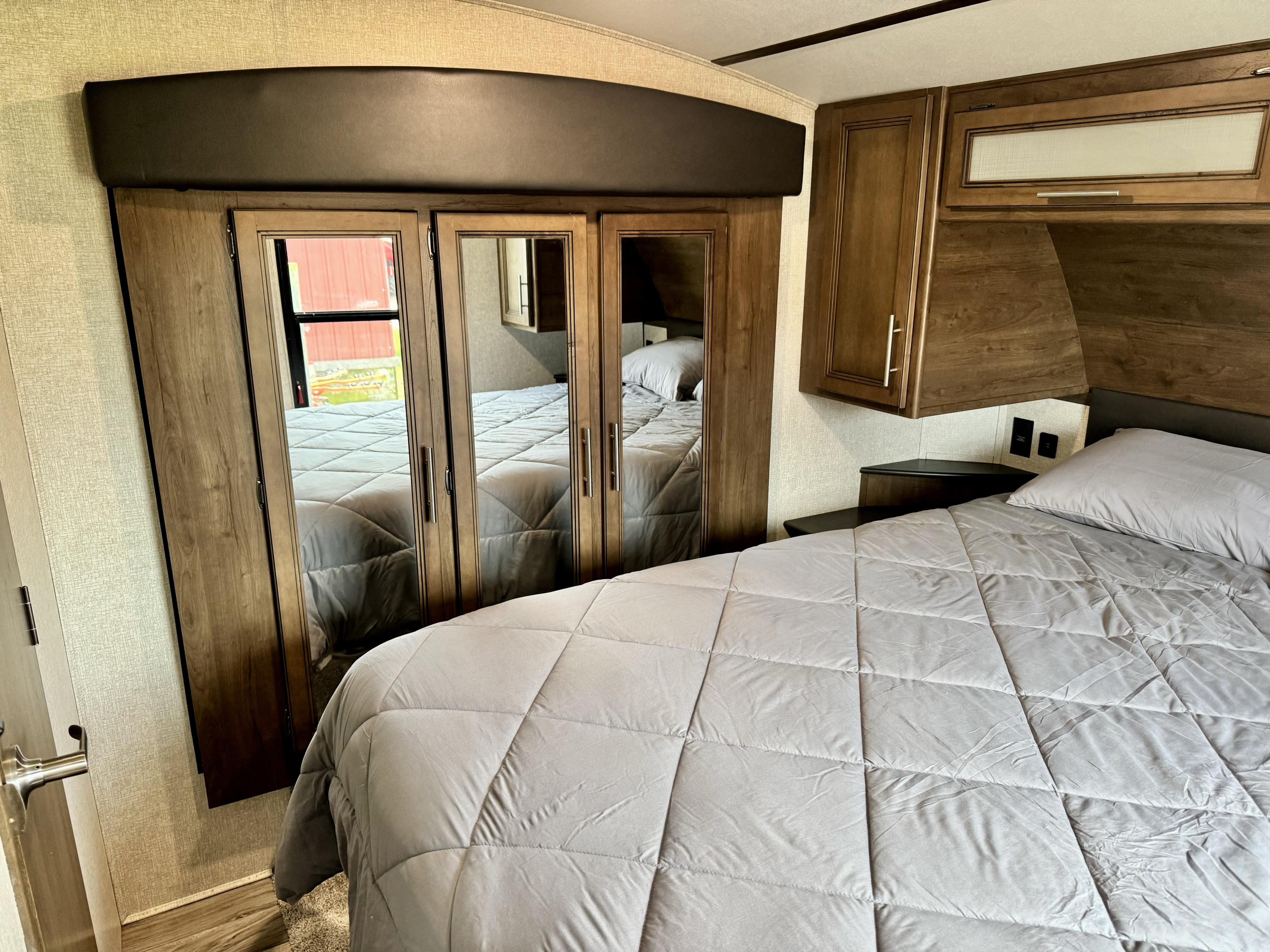Inside an RV rental: a cozy bedroom features a gray comforter, built-in cabinets, and mirrored wardrobe.. Keystone RV Cougar 2020