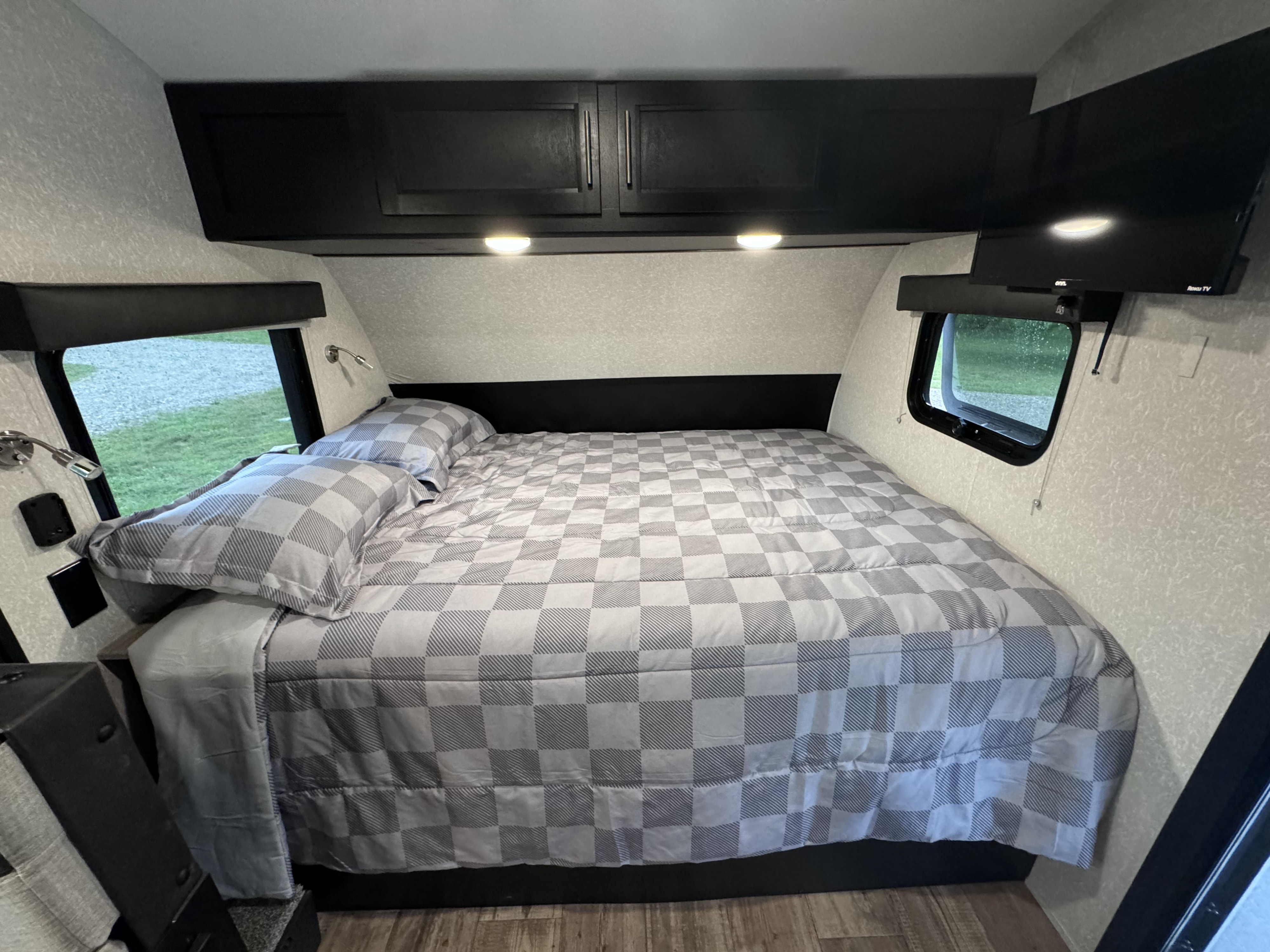Cozy RV rental bedroom featuring a checkered bed, overhead cabinets, reading lights, and windows. Perfect for travel.. Forest River Cherokee Wolf Pup Black Label 2022