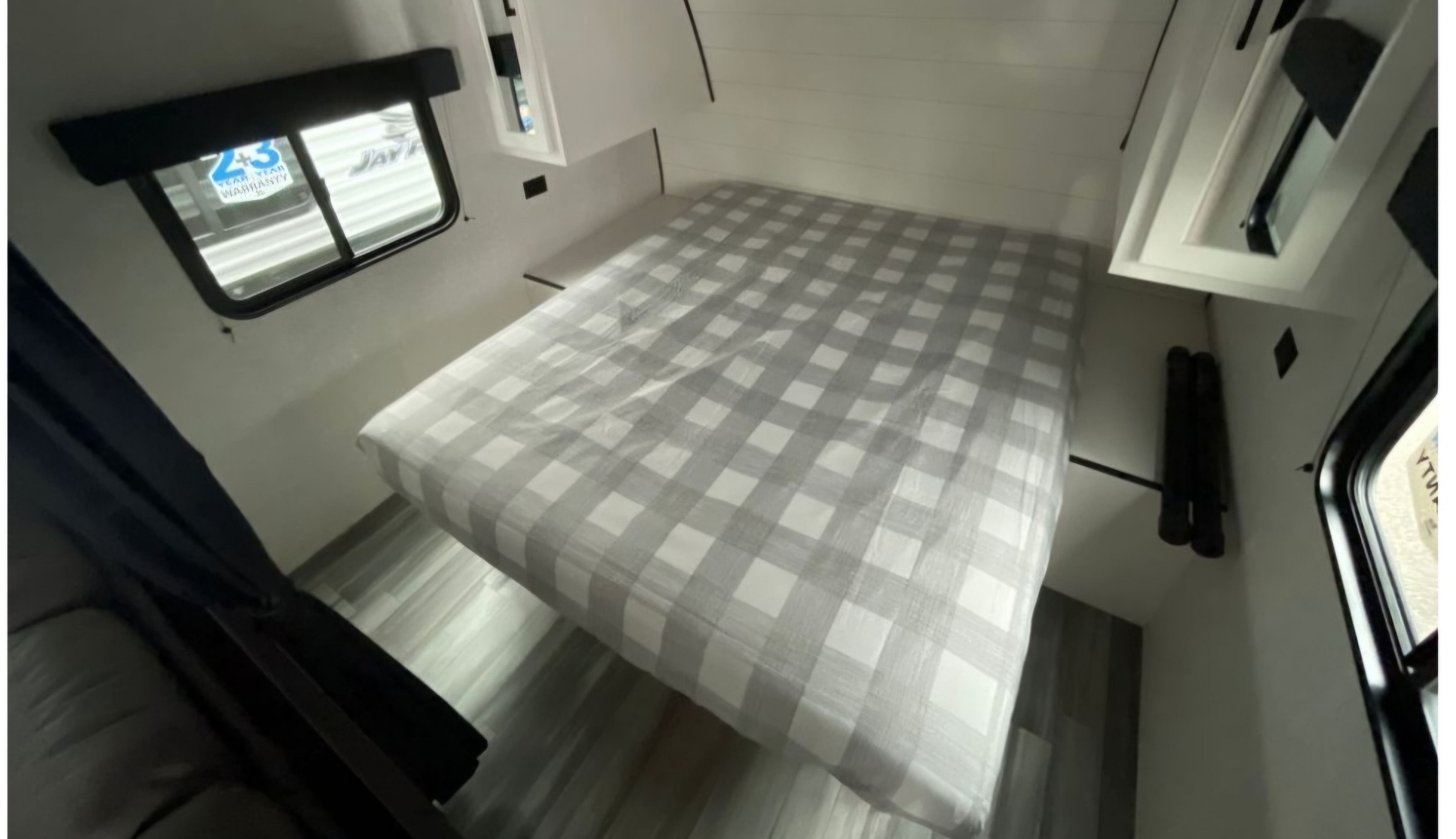 Spacious RV rental bedroom featuring a large bed with gray and white checkered bedding, bright white walls, and a visible window.. Jayco Jay Flight SLX 2024