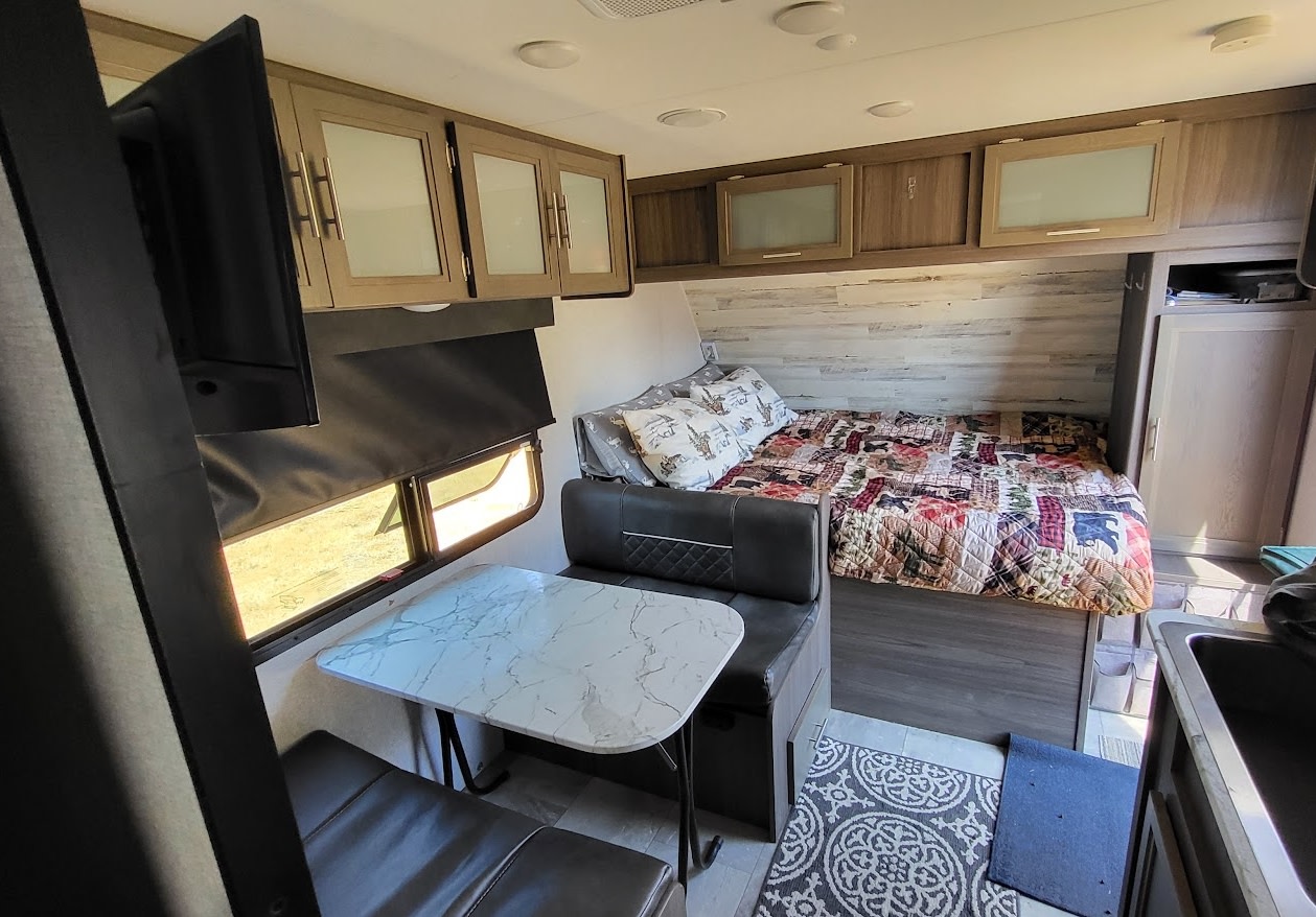 Spacious RV rental interior with a cozy bed, dinette, kitchen, and window view for comfortable travel.. Dutchmen Kodiak Cub 2021
