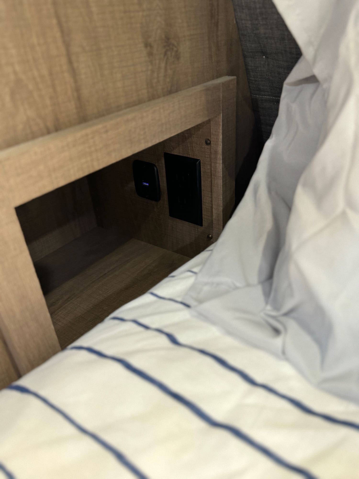 RV rental: Wooden built-in nightstand with power and USB outlets next to a bed with striped bedding.. Grand Design Imagine 2022