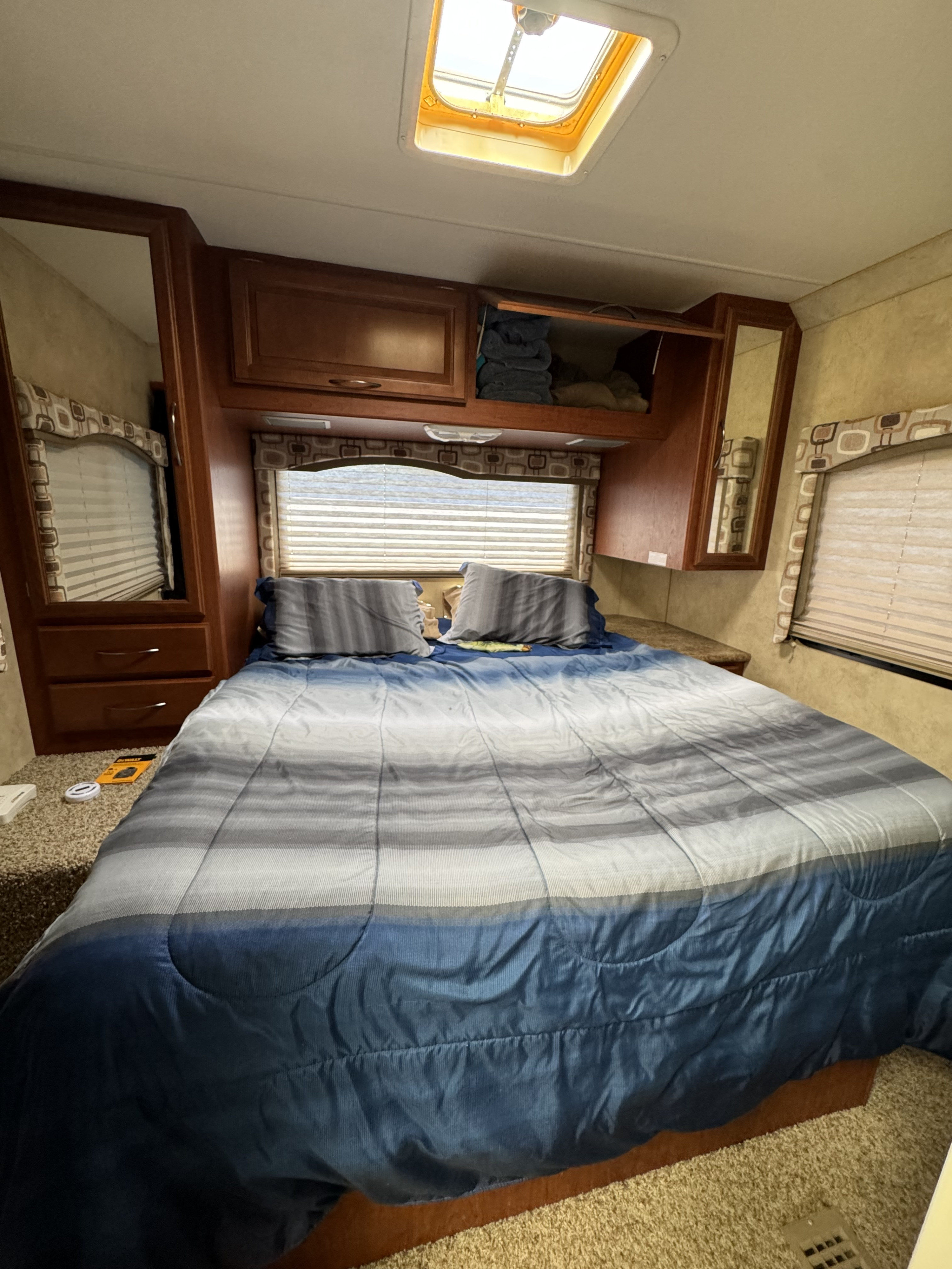Spacious RV rental bedroom with a comfortable bed, overhead cabinets, windows, and skylight for natural light. Perfect for travel.. Thor Motor Coach Four Winds 2013