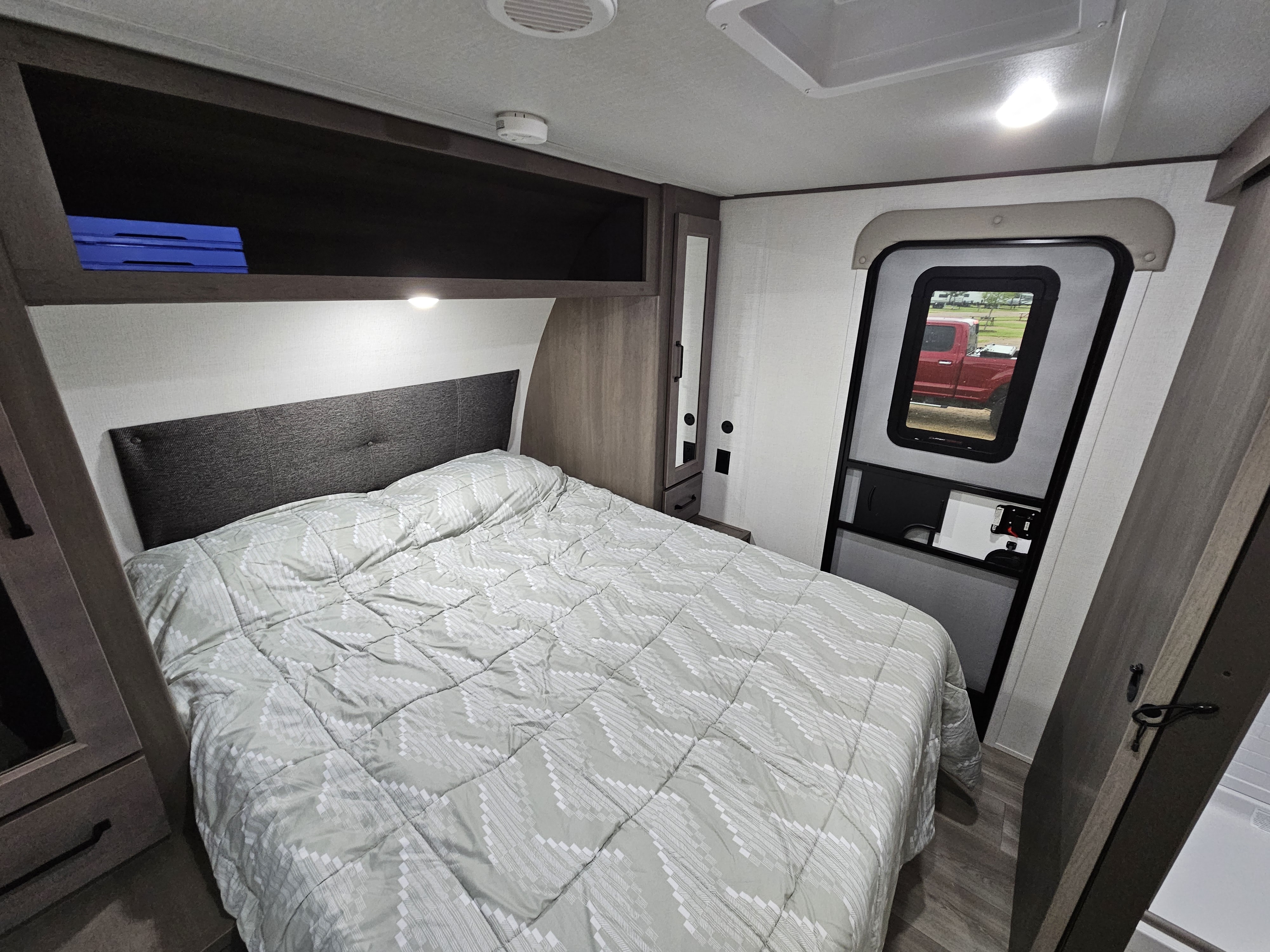 Cozy RV rental bedroom featuring a bed with patterned comforter, overhead cabinets, and an exterior door view.. Grand Design Transcend Xplor 2024