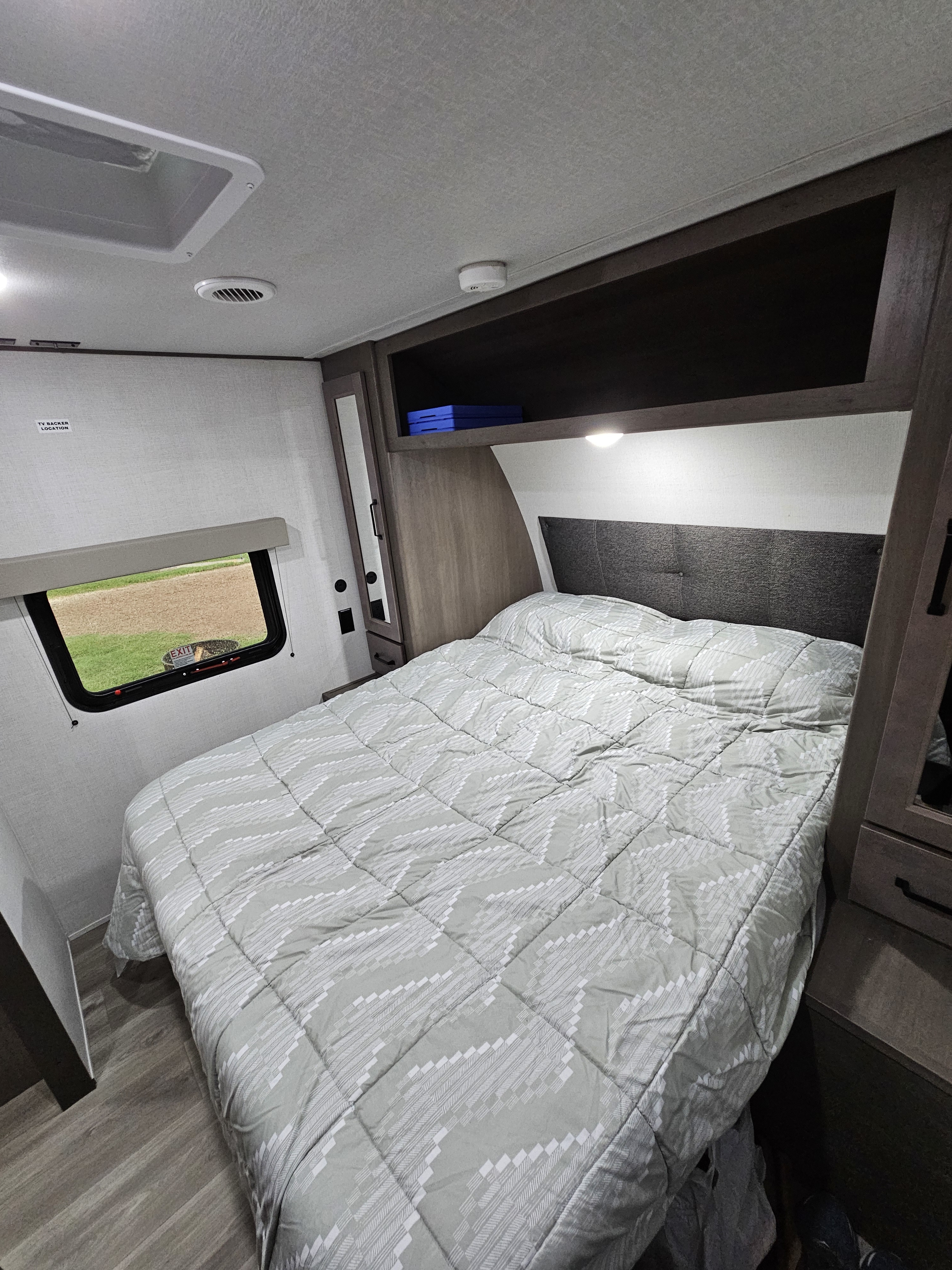 RV rental bedroom with a cozy bed, headboard, overhead storage, window view, and ceiling amenities for comfort.. Grand Design Transcend Xplor 2024