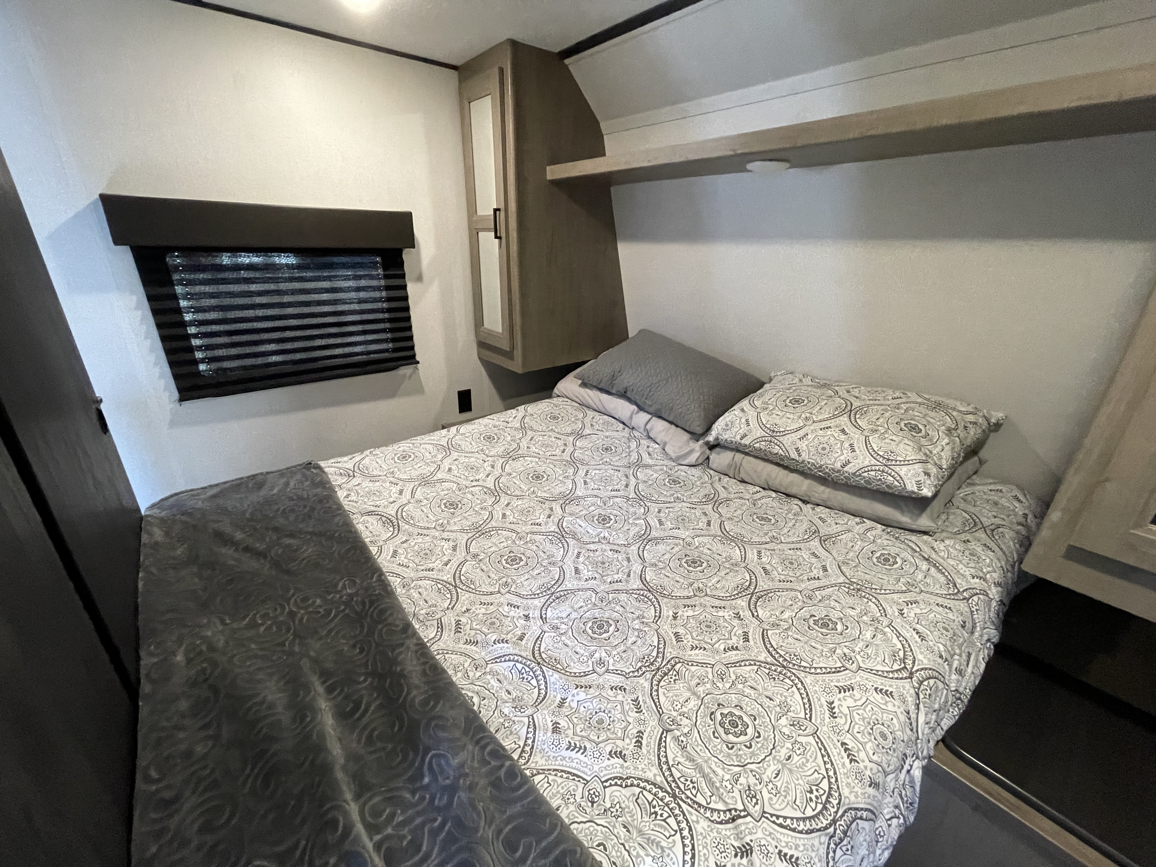 A cozy bedroom inside an RV rental, featuring a patterned bedspread, blinds, and cabinet storage for comfortable travel.. Keystone RV Hideout 2021