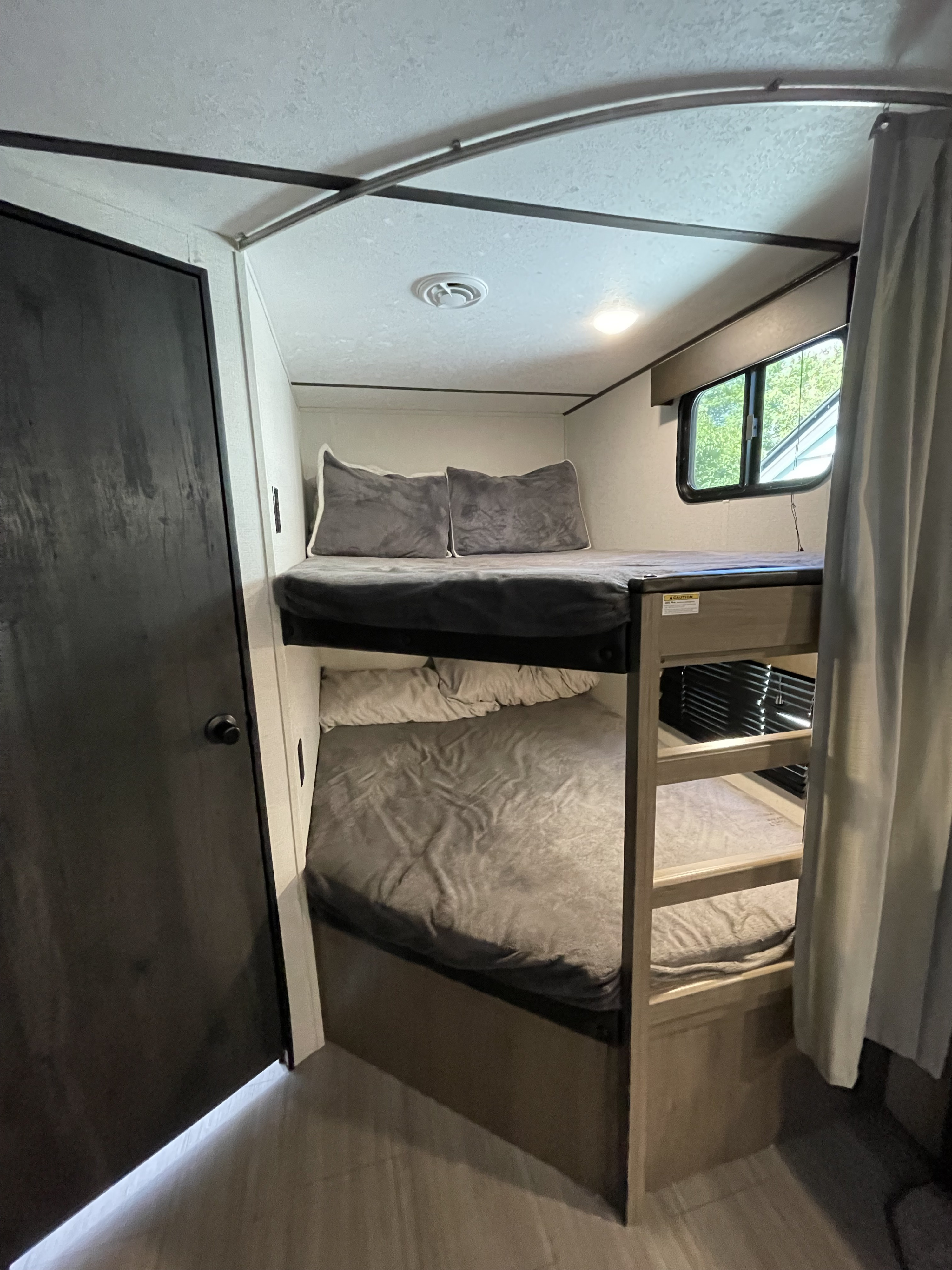 Inside an RV rental: cozy bunk beds with soft grey bedding, a window, and privacy curtain. Ideal for family travel.. Keystone RV Hideout 2021