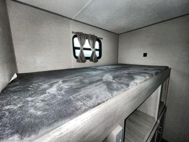 This RV rental bunk bed offers a comfortable sleeping space with a soft grey mattress and a small window for natural light.. Forest River Aurora Aurora 2022