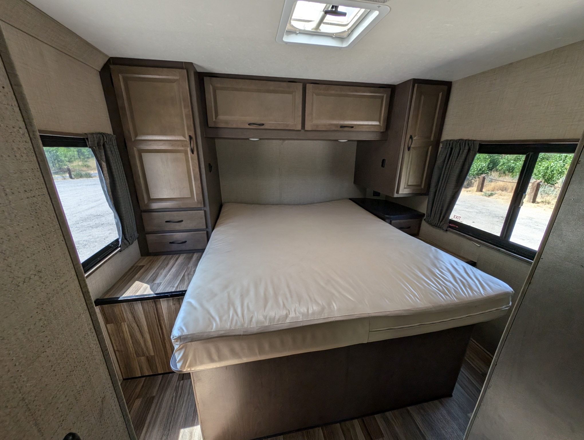 RV rental bedroom: large bed, wooden overhead & side cabinets, side windows revealing outdoor views, plus a ceiling skylight.. Thor Majestic 2019