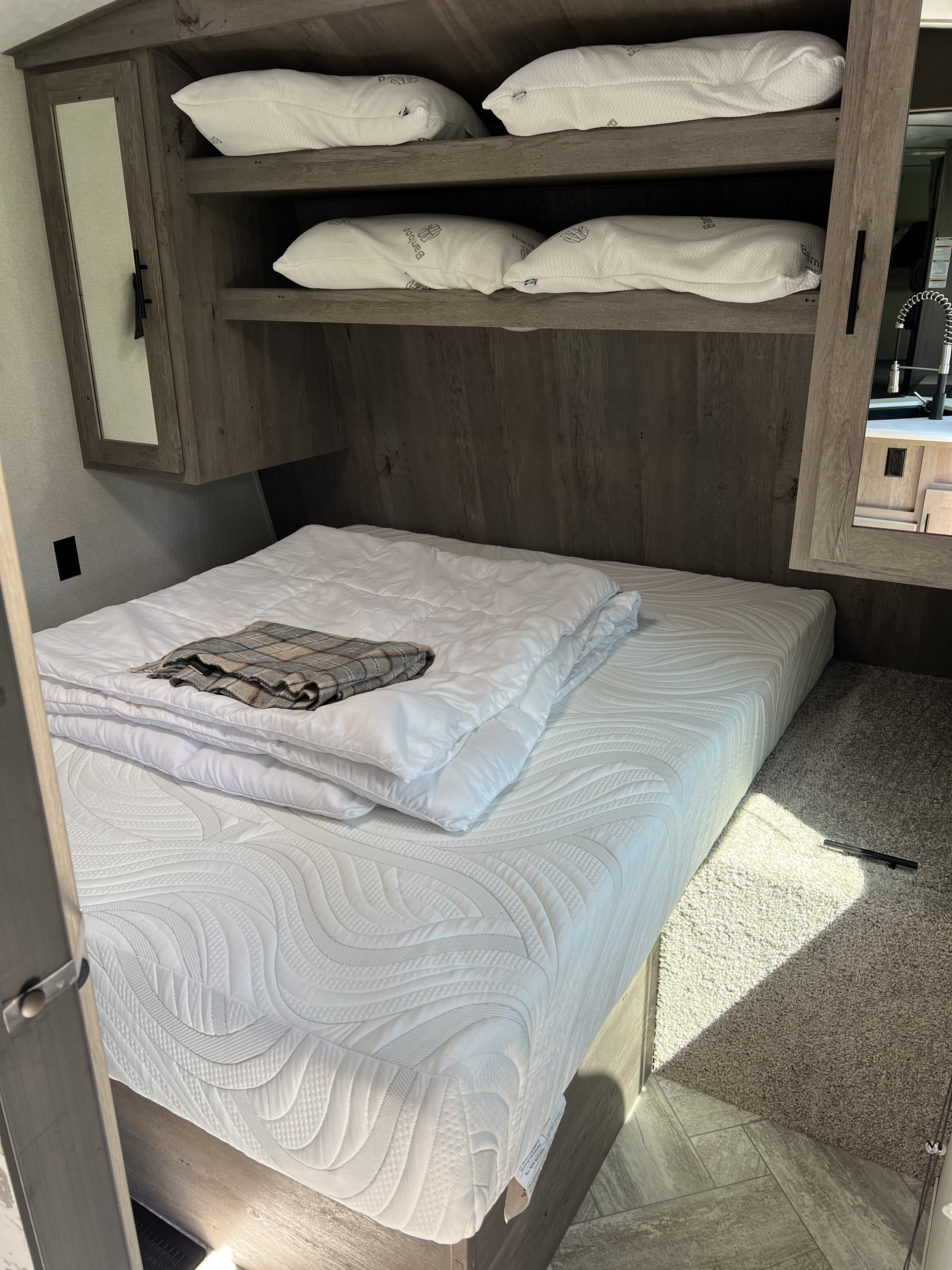 RV rental's inviting bedroom features a new mattress, soft bedding, & four Bamboo pillows on shelves.. Keystone RV Springdale 2021