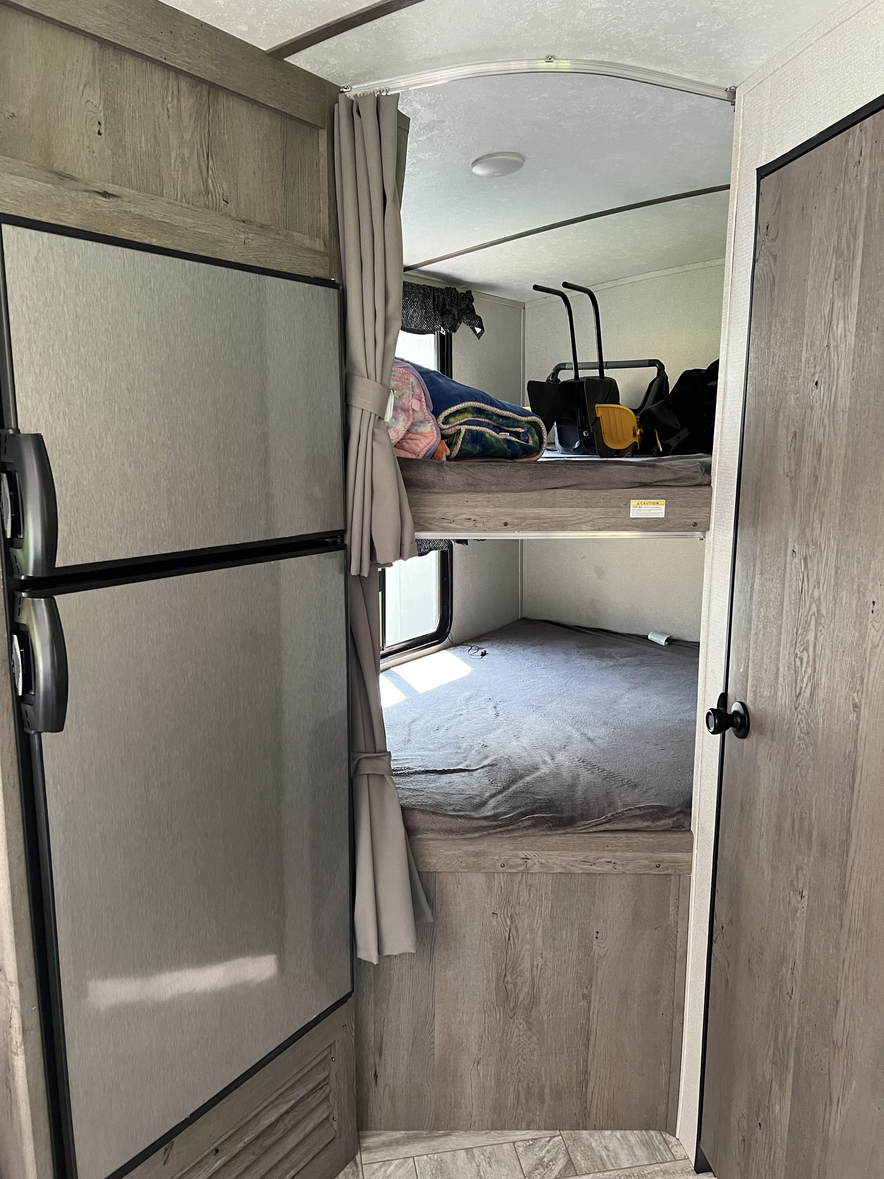 RV rental interior featuring a modern refrigerator on the left and cozy bunk beds with privacy curtains on the right.. Keystone RV Springdale 2021