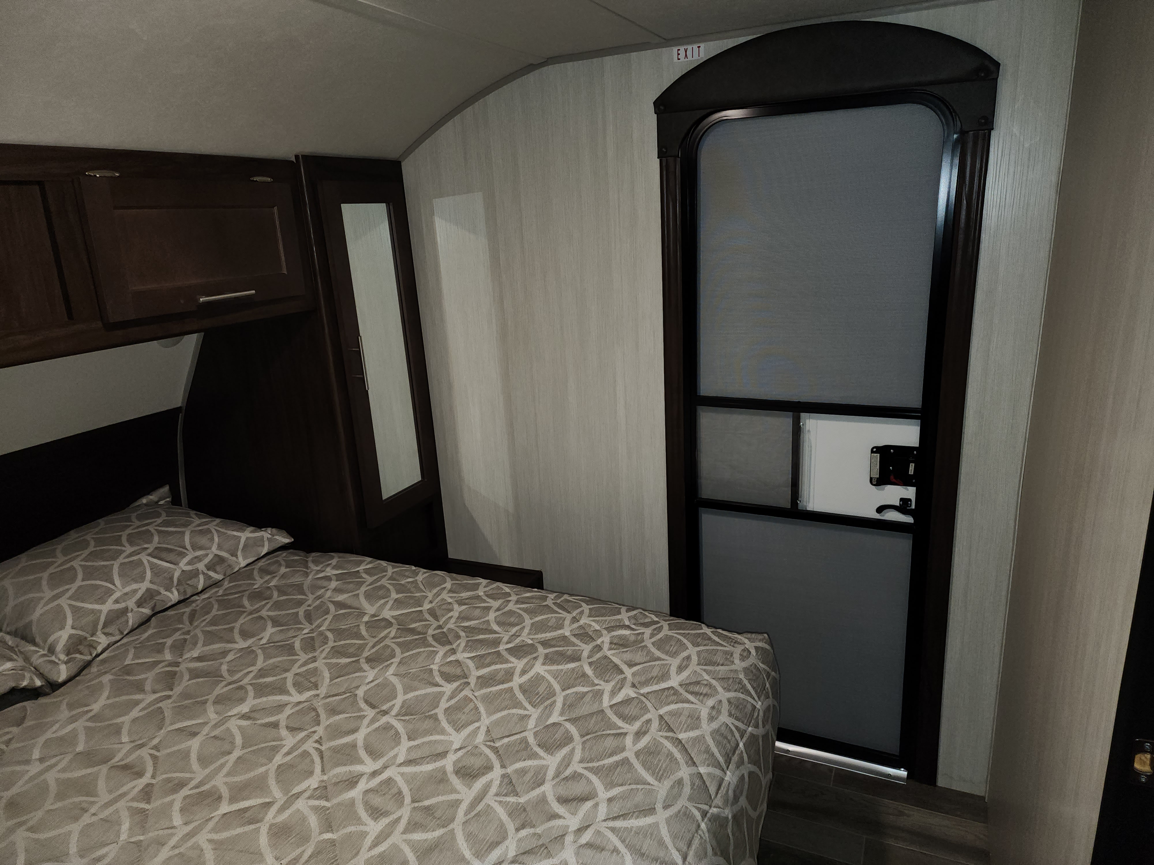Bedroom inside an RV rental, featuring a cozy bed with patterned covers, overhead storage, and an exit door.. Forest River Cherokee 2020