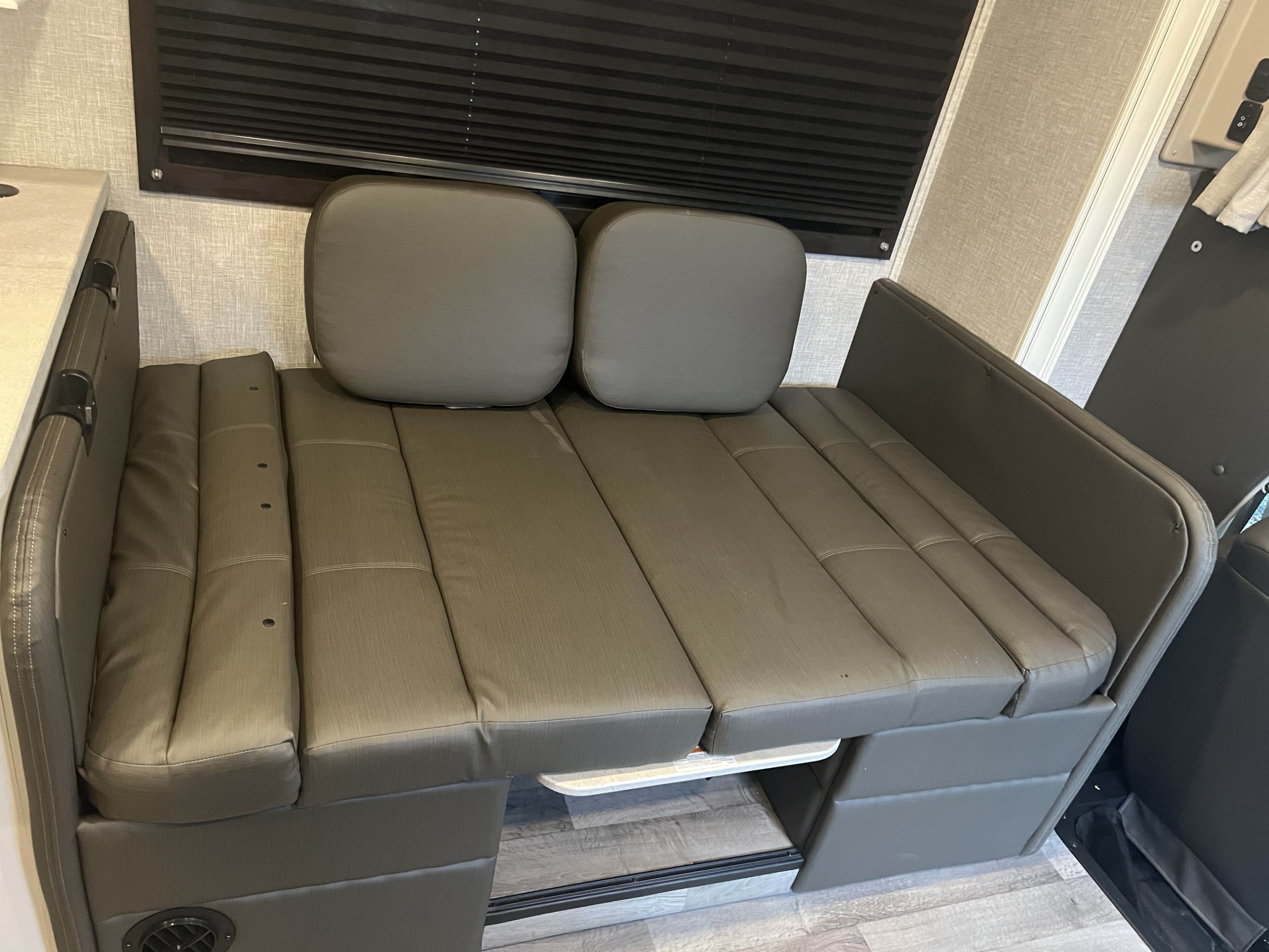 RV rental interior showcasing a multi-functional dinette/sofa with convertible bed cushions & window blinds.. Entegra Coach Odyssey 2023