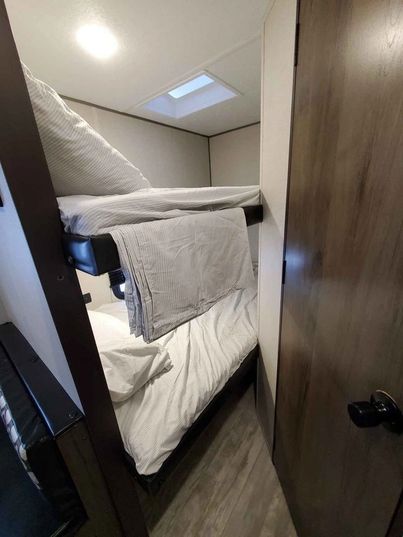 This RV rental features compact, neatly made bunk beds with a skylight, creating a cozy sleeping space beside a dark wood door.. Prime Time Avenger 2021