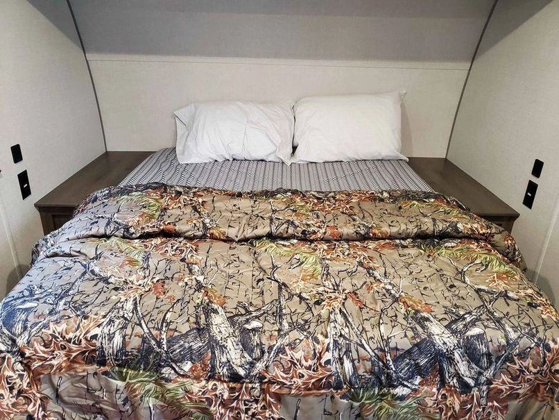 Inside an RV rental: a cozy bedroom with a bed, white pillows, and a unique camouflage comforter.. Prime Time Avenger 2021