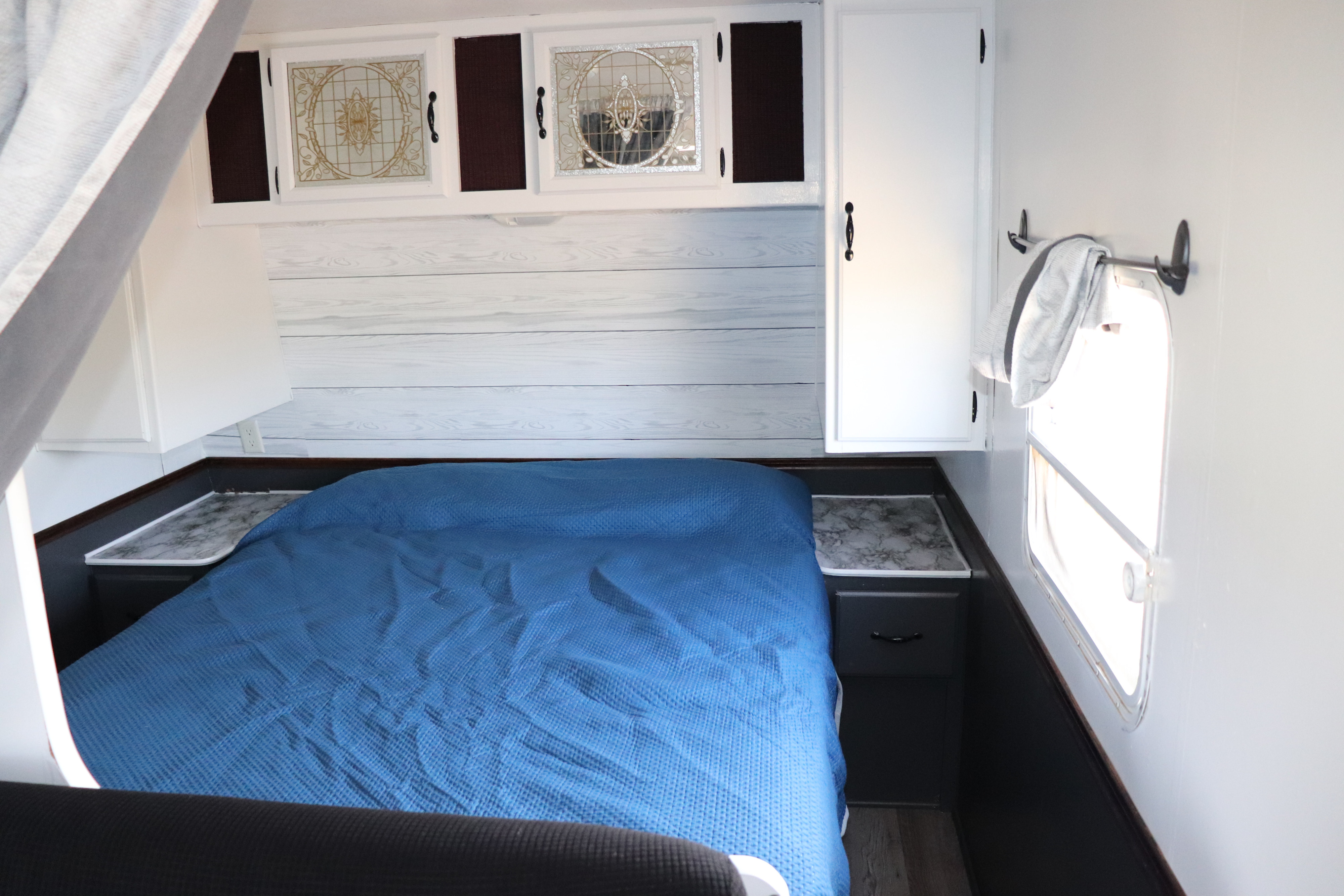 RV rental bedroom with blue bed, white shiplap wall, and modern overhead cabinets.. Fleetwood Mallard 2000
