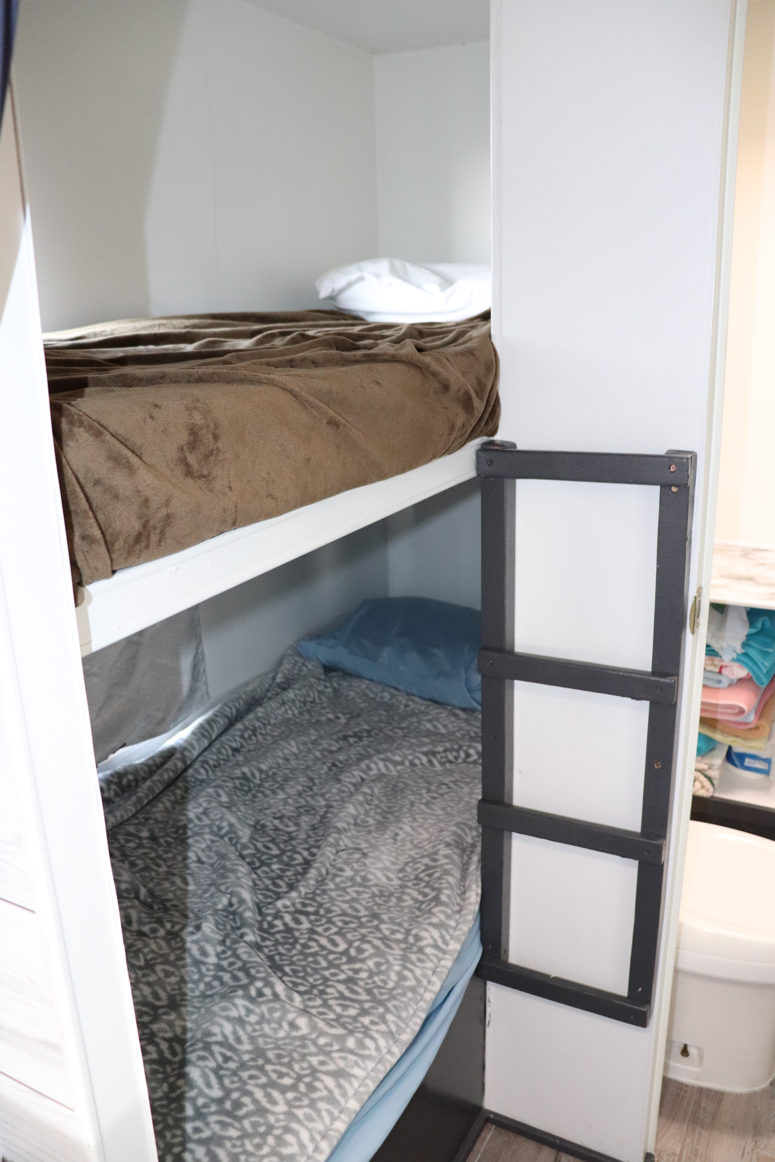 Bunk beds with a ladder in an RV rental. Top bed has a brown blanket, bottom a gray one. Toilet nearby.. Fleetwood Mallard 2000
