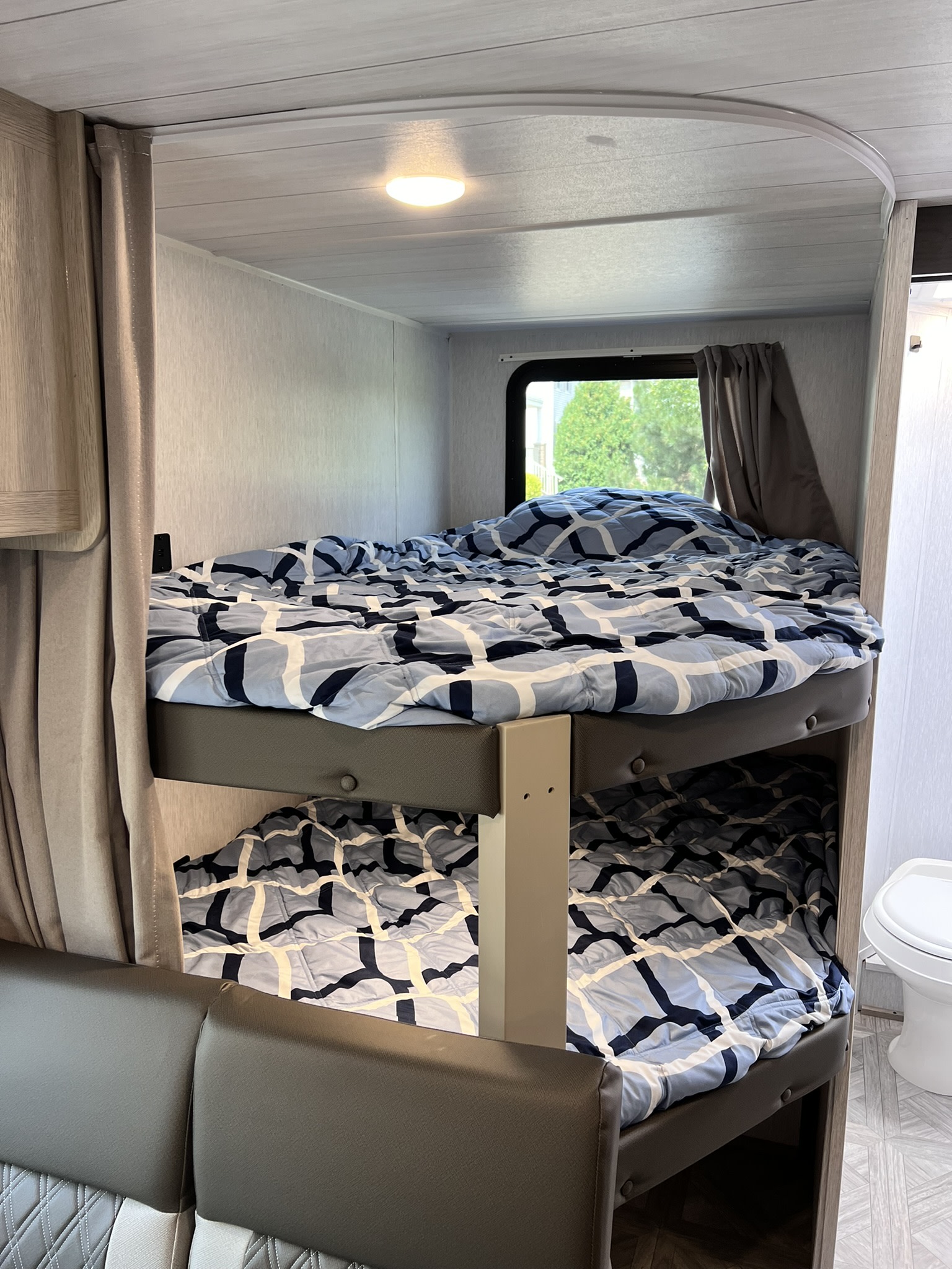Cozy bunk beds in an RV rental, featuring blue patterned comforters, a window, and privacy curtains. Great for travel.. Forest River Salem Cruise Lite 2024