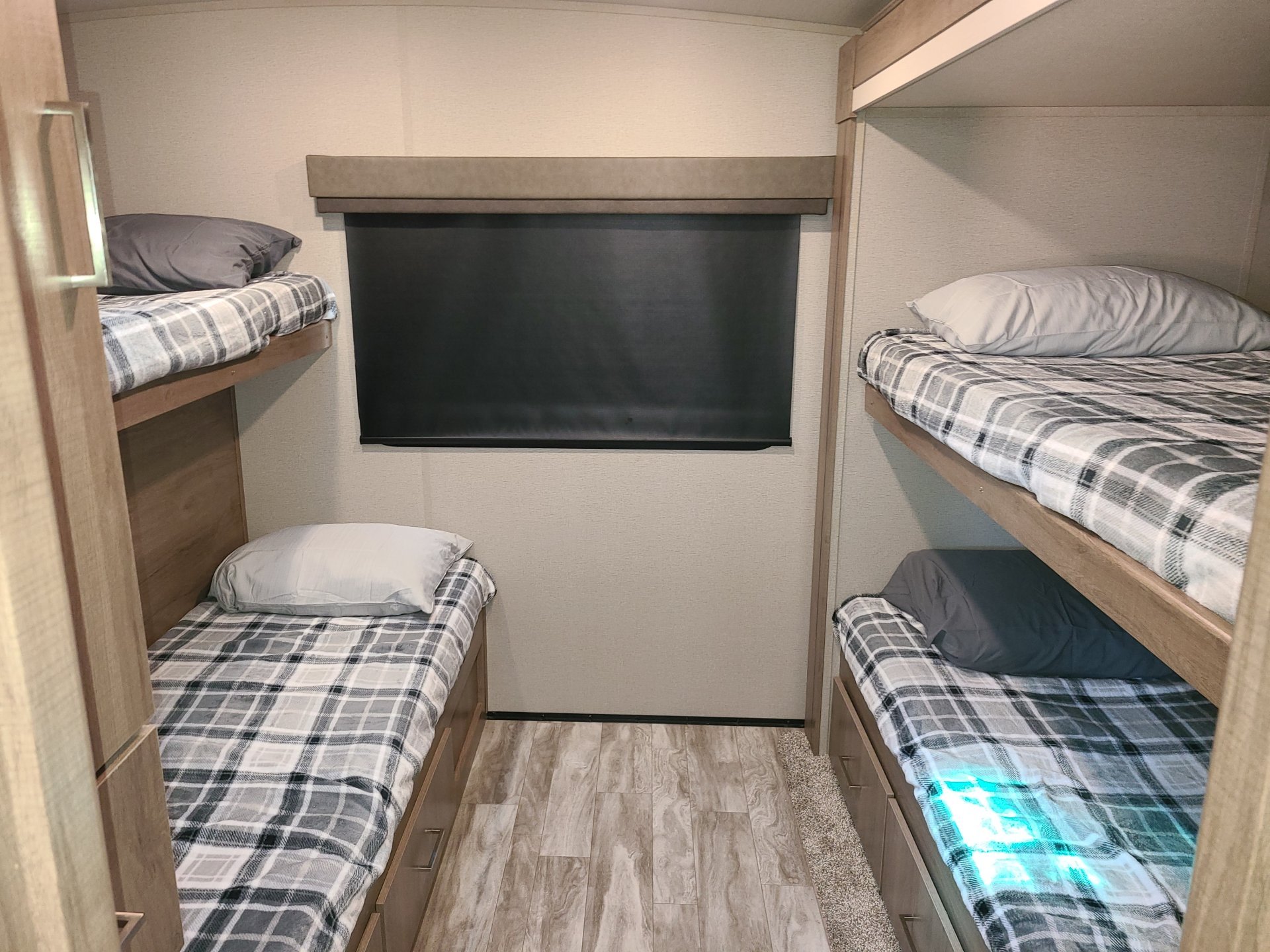 Cozy RV rental interior showing four bunk beds with plaid blankets and under-bed storage drawers.. Grand Design Imagine 2023